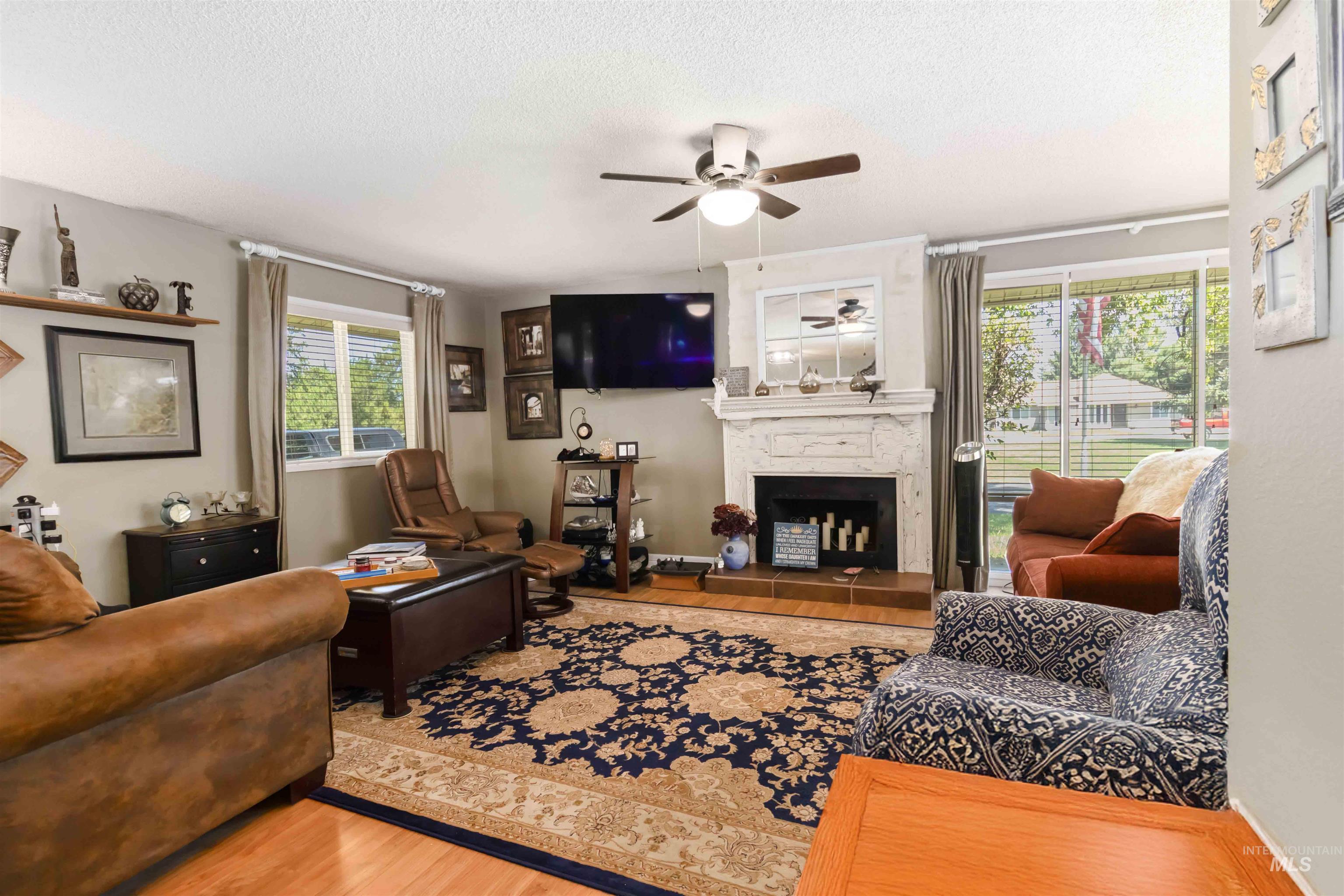 Living room featuring a fireplace, wood finished floors, ceiling fan, and a textured ceiling