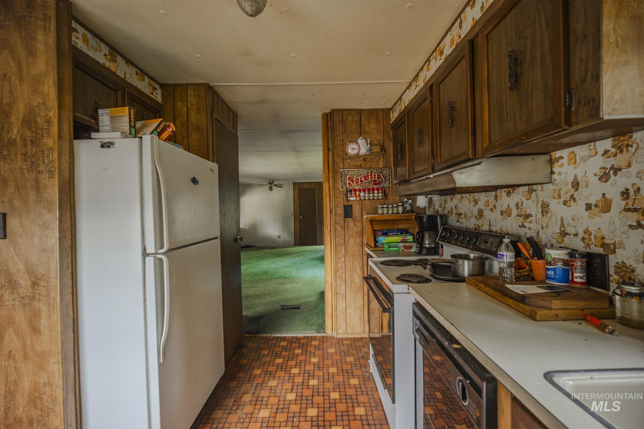 Kitchen featuring white appliances, light countertops, dark brown cabinetry, and under cabinet range hood
