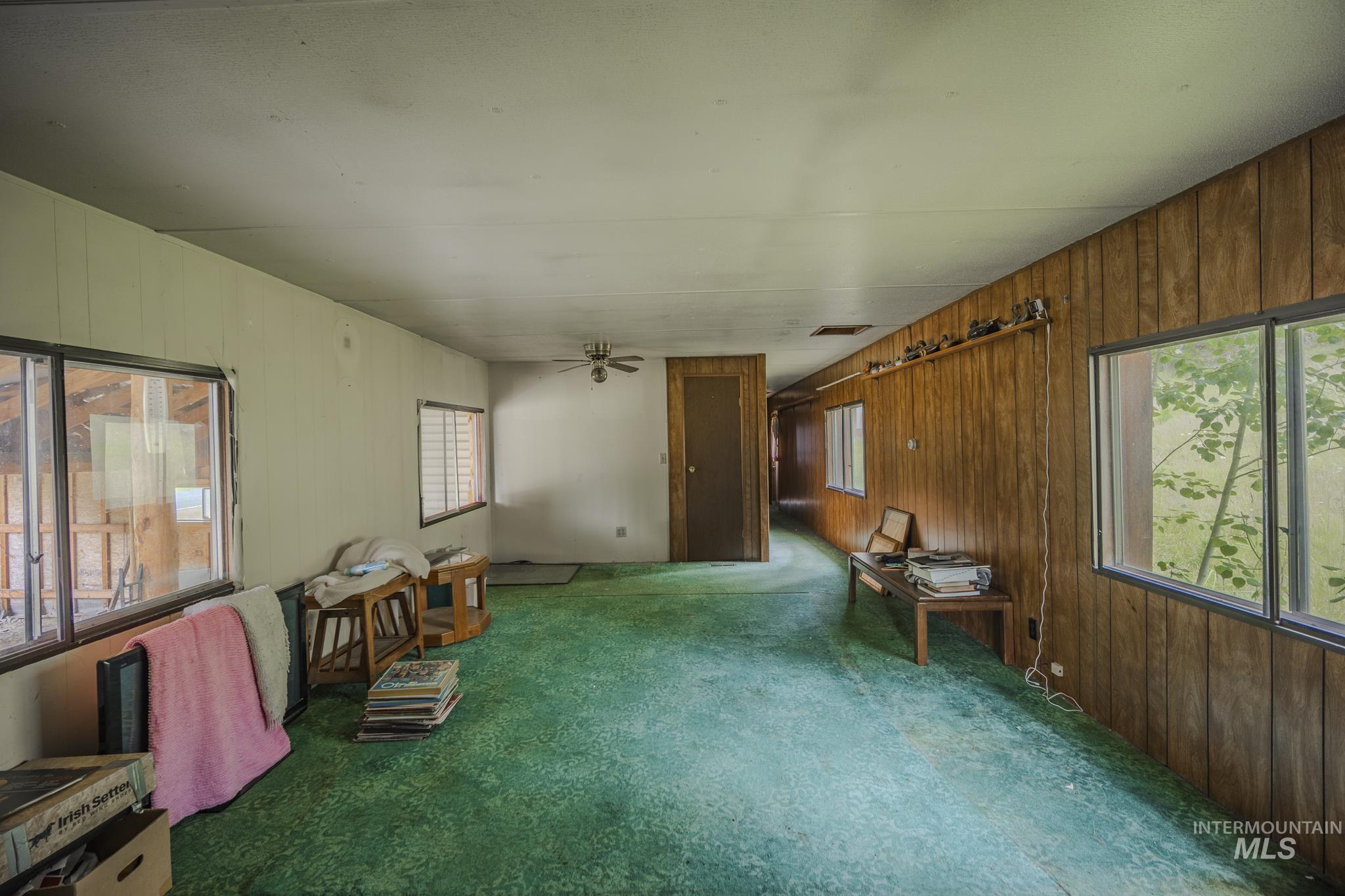 Living area with wooden walls, carpet floors, and ceiling fan
