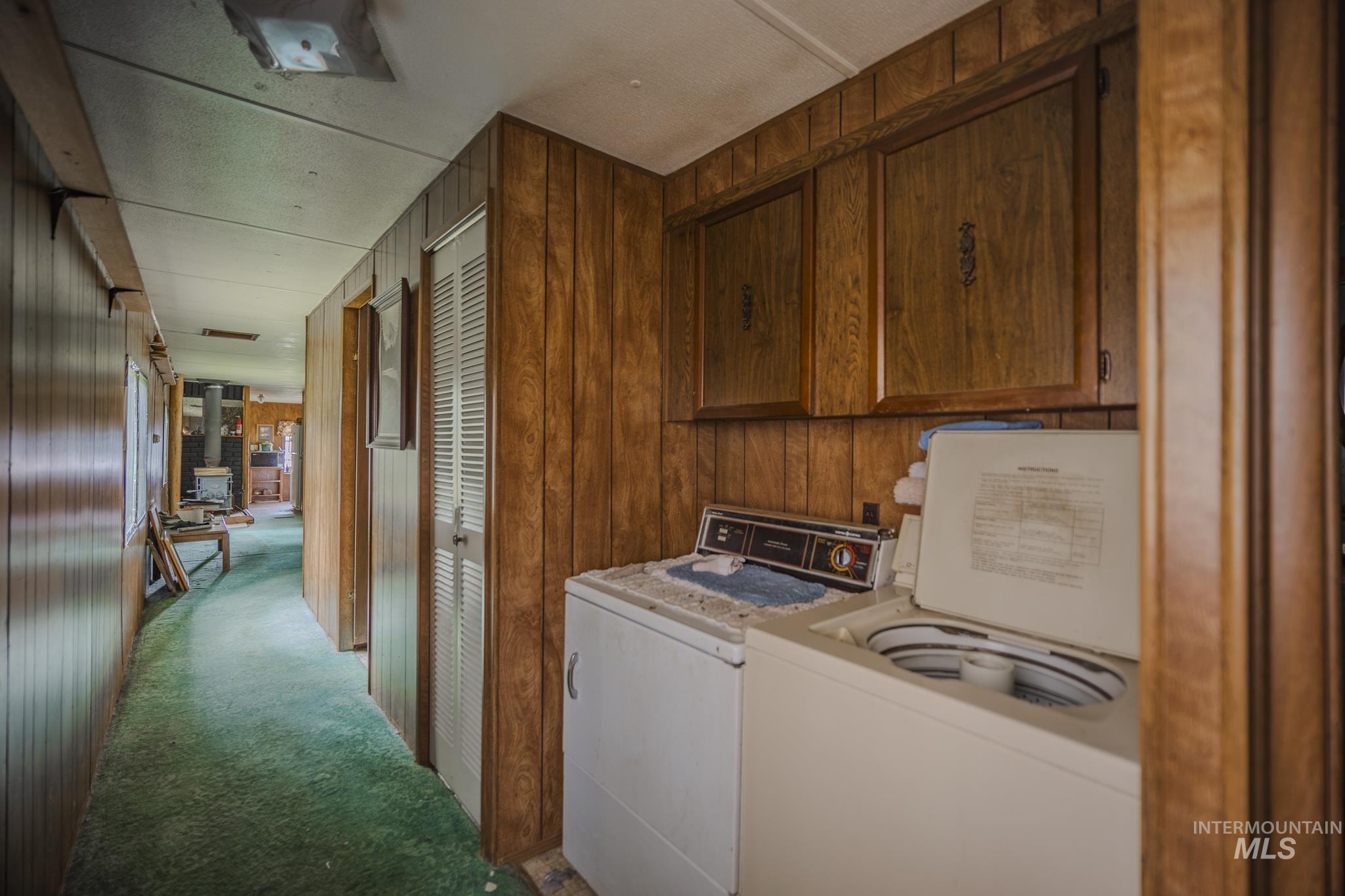 Laundry room with light colored carpet, washing machine and dryer, wood walls, and cabinet space