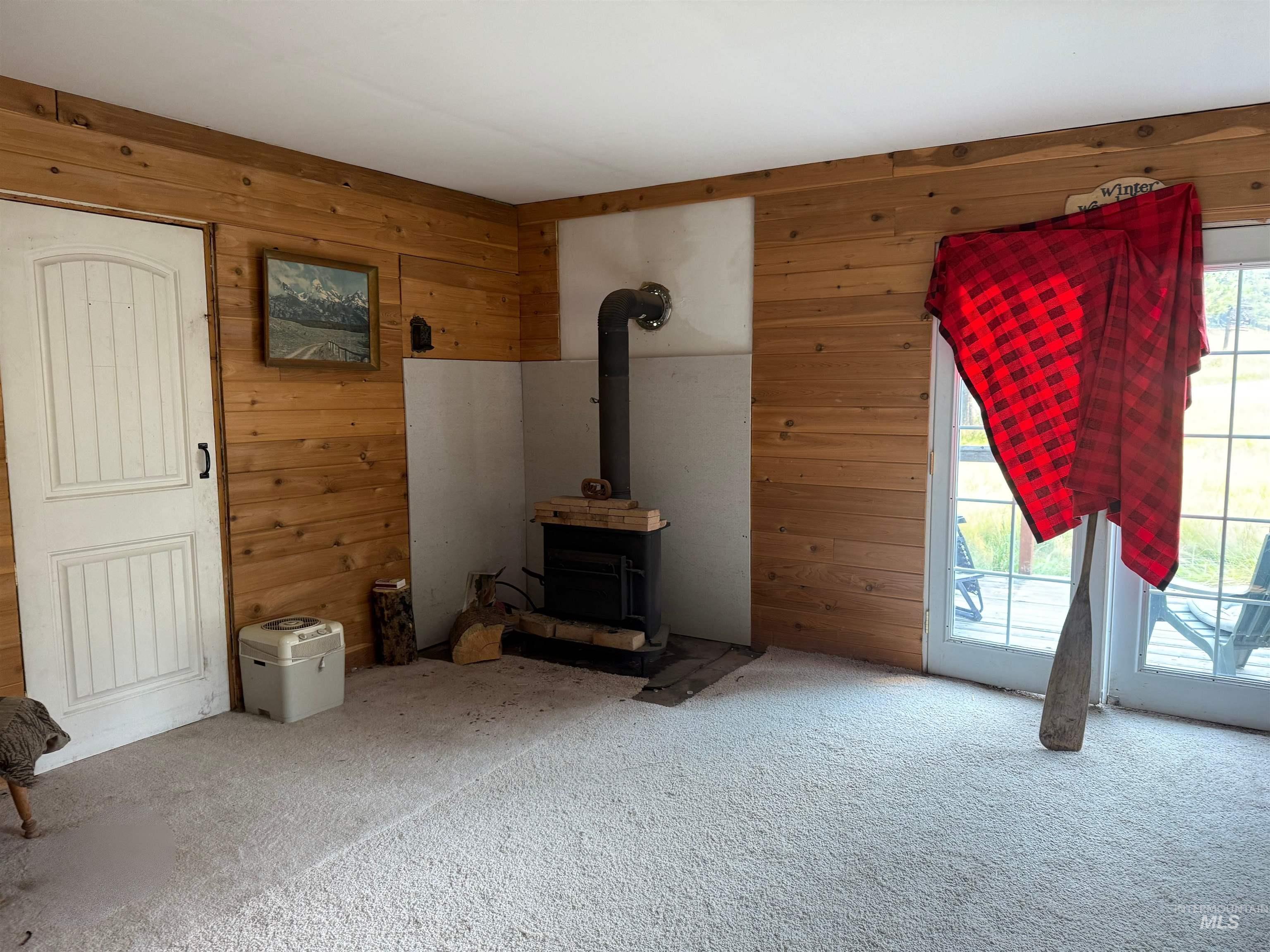 Unfurnished living room featuring wooden walls, carpet, and a wood stove