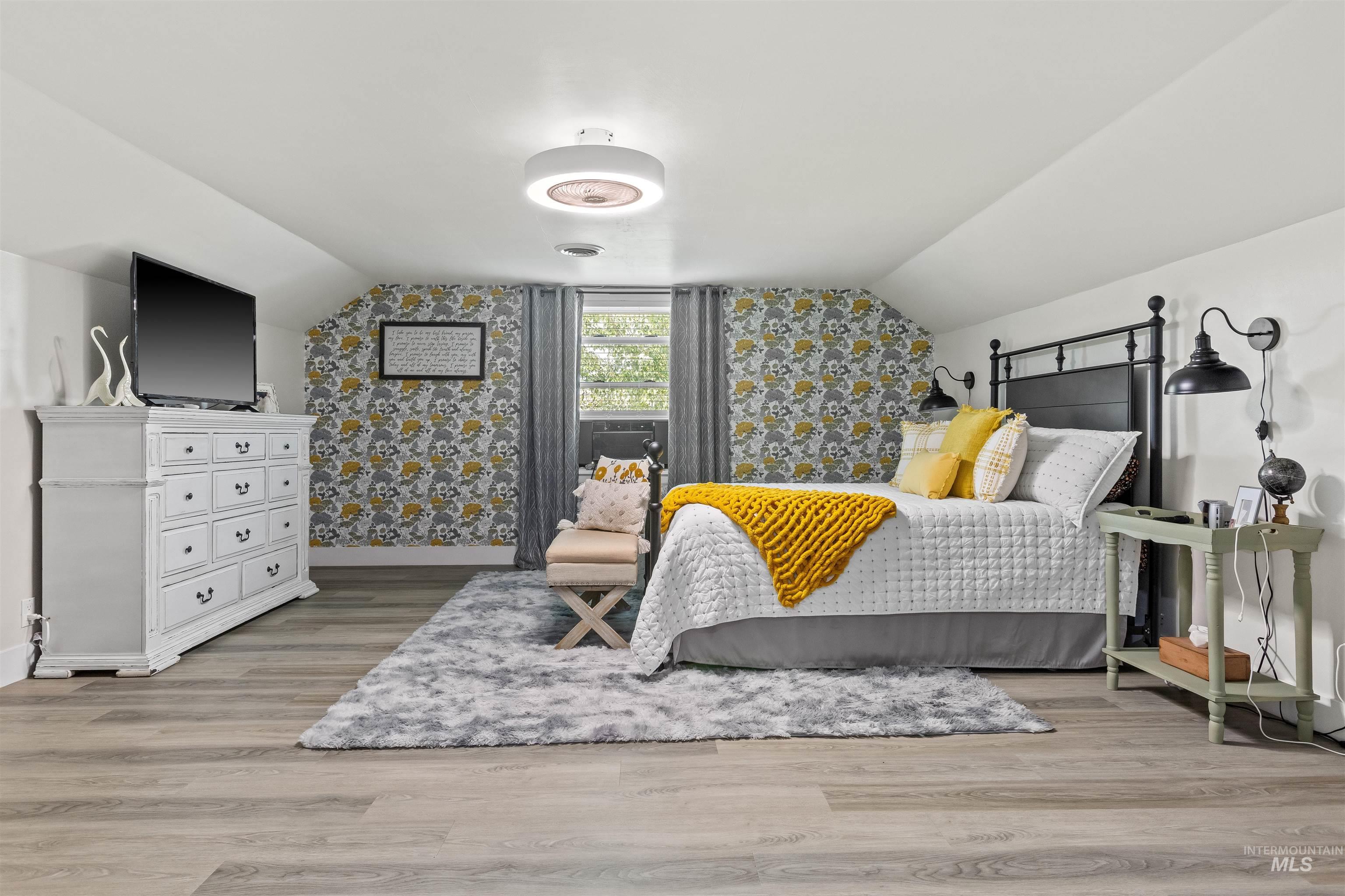 Bedroom featuring vaulted ceiling, light wood-type flooring, and wallpapered walls