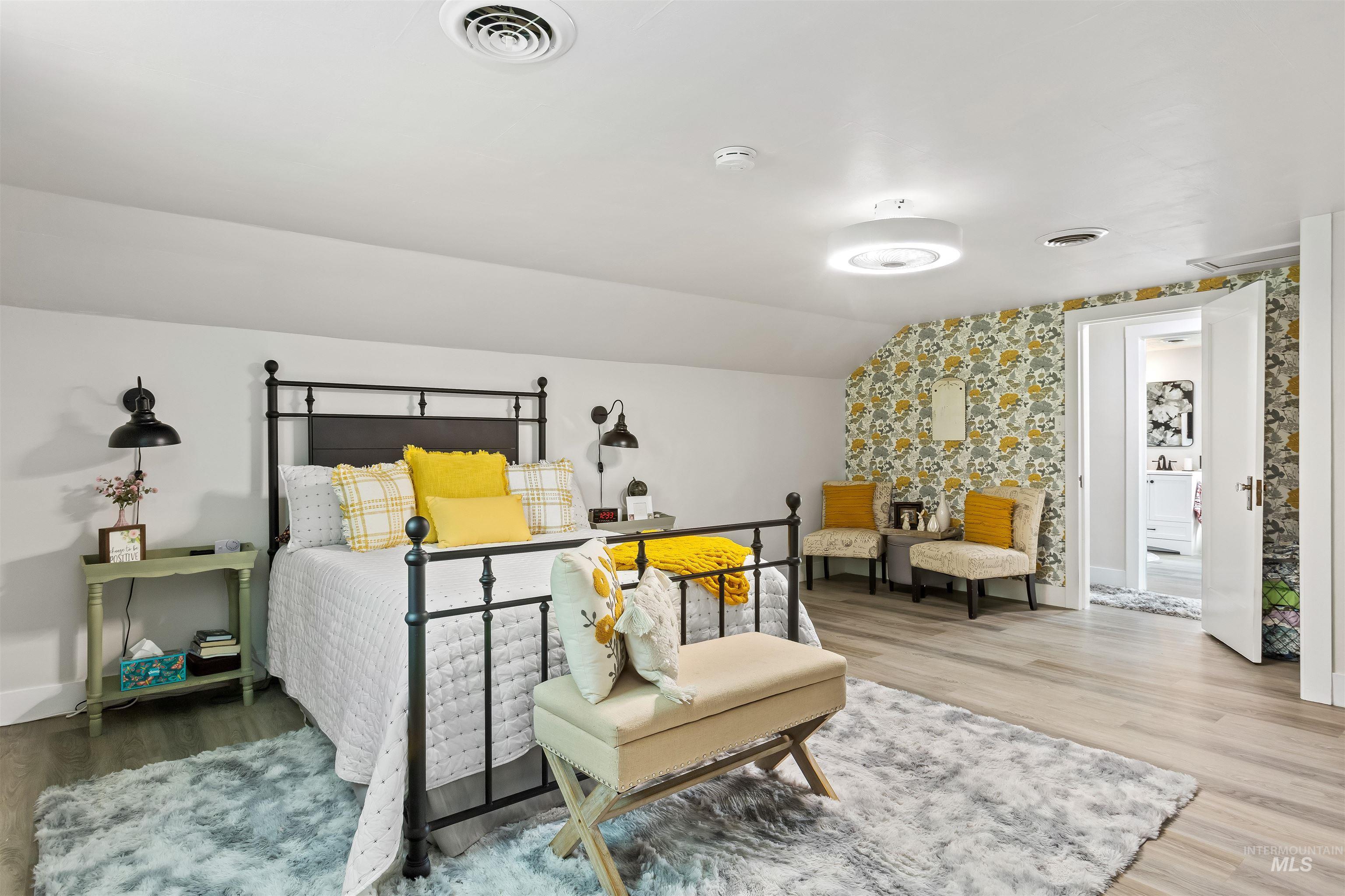 Bedroom featuring wood finished floors, wallpapered walls, and lofted ceiling
