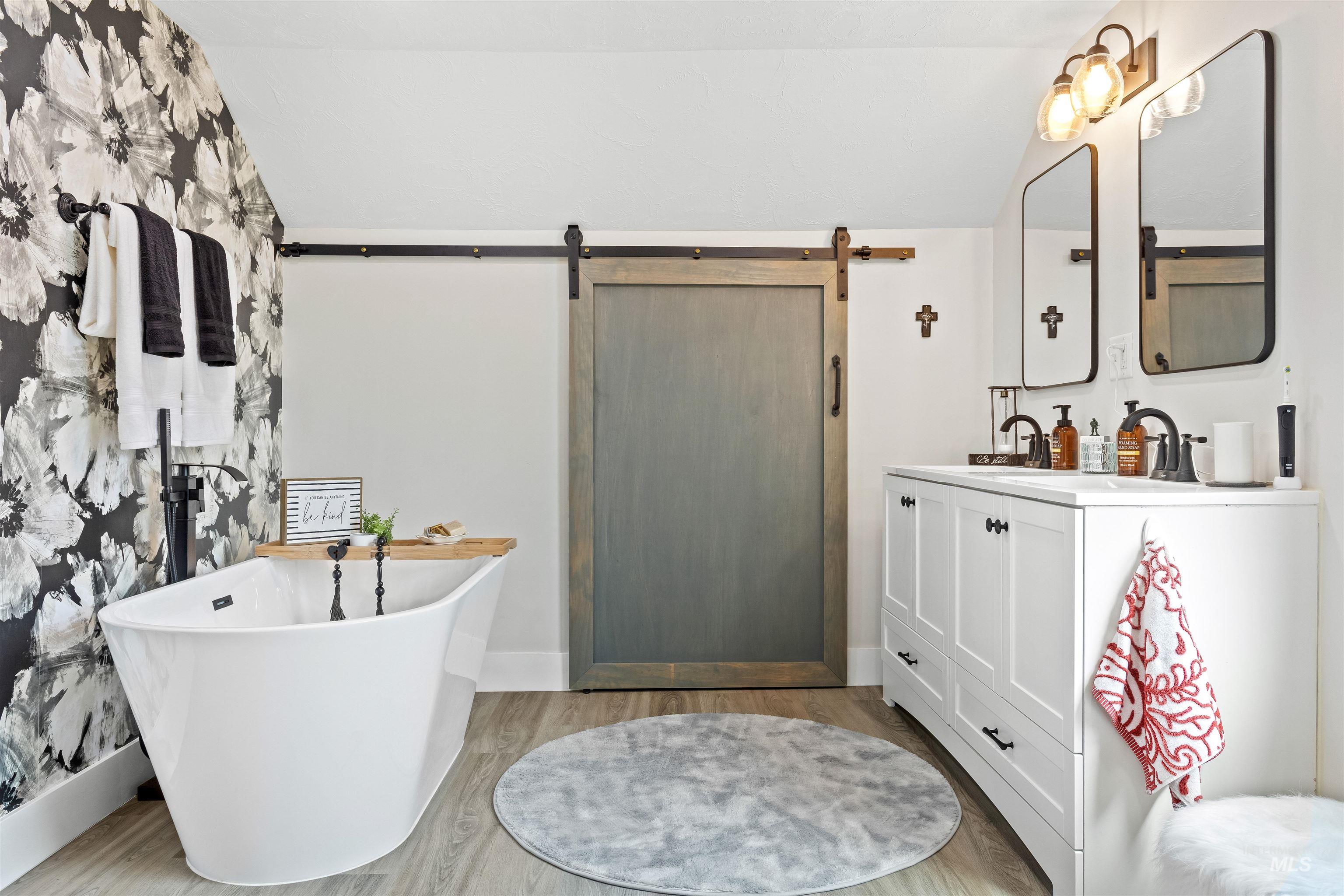 Bathroom with vaulted ceiling, vanity, a freestanding tub, and light wood-type flooring