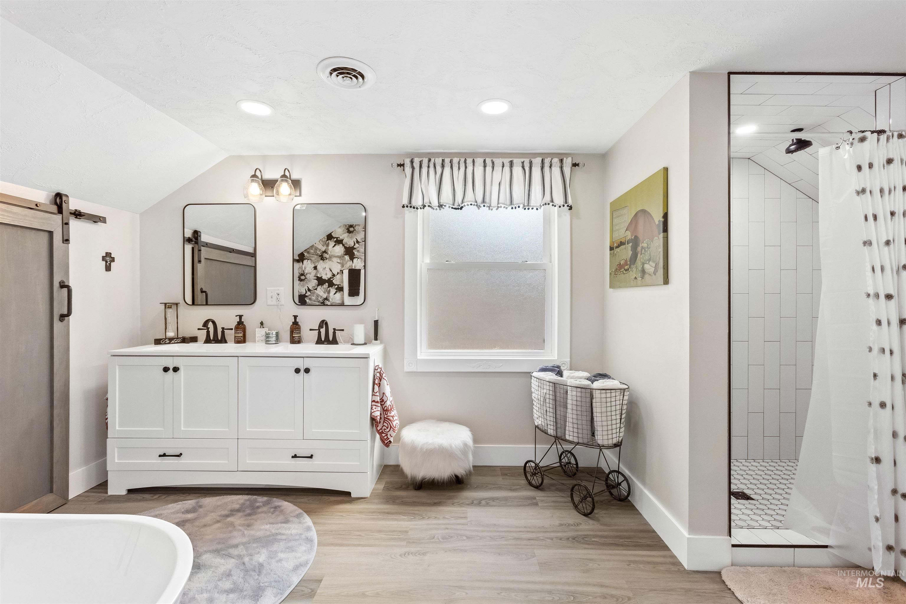 Bathroom featuring a stall shower, double vanity, light wood finished floors, lofted ceiling, and a soaking tub