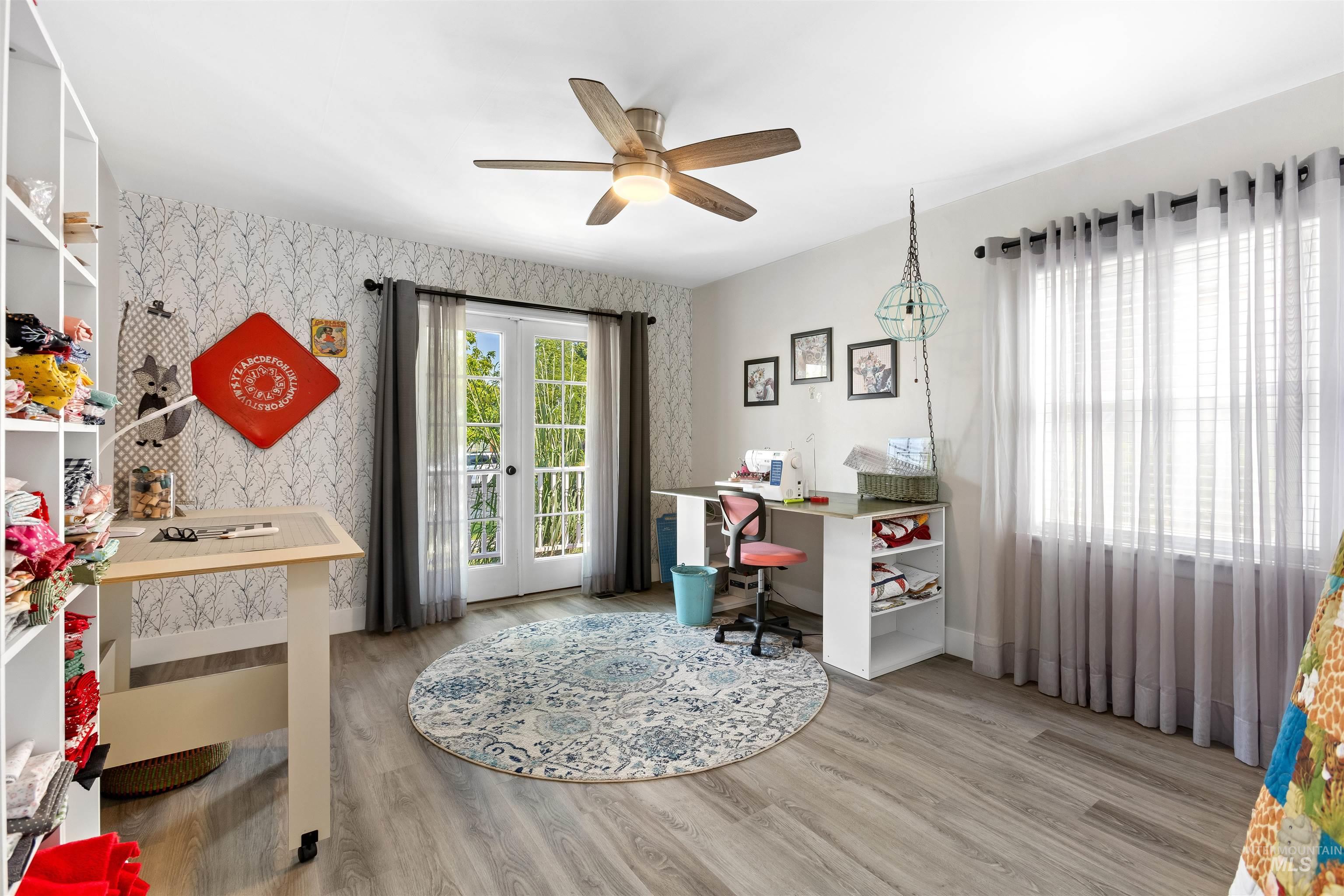 Office area with wallpapered walls, light wood-style flooring, a ceiling fan, and french doors