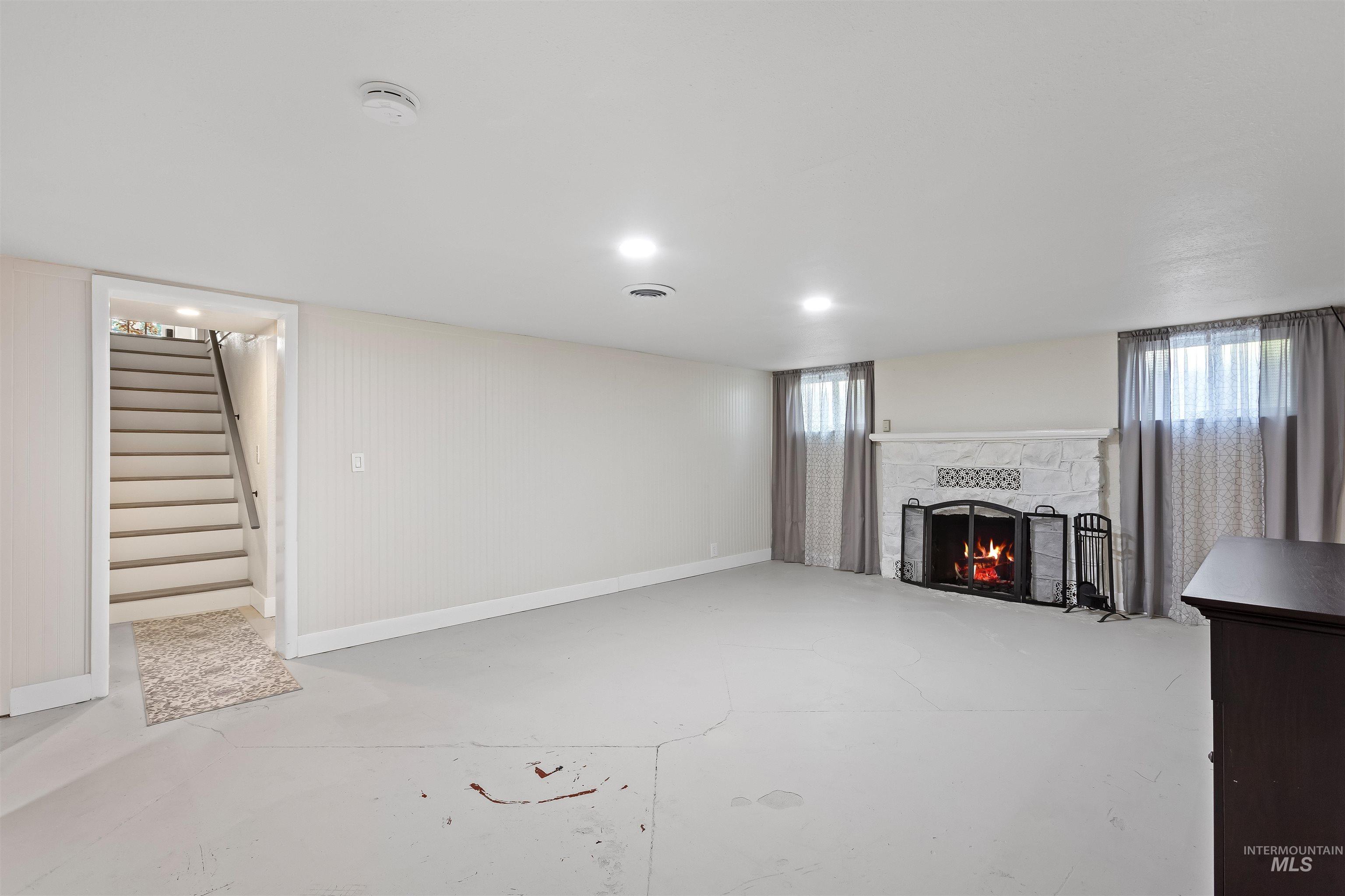 Unfurnished living room featuring a stone fireplace, stairway, concrete floors, and recessed lighting