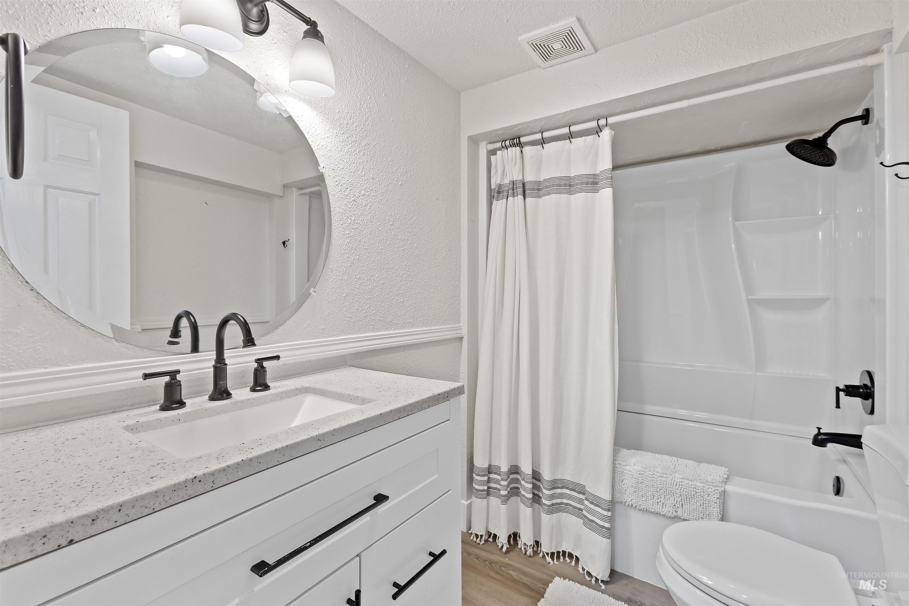 Bathroom featuring a textured wall, shower / bathtub combination with curtain, vanity, and light wood-type flooring