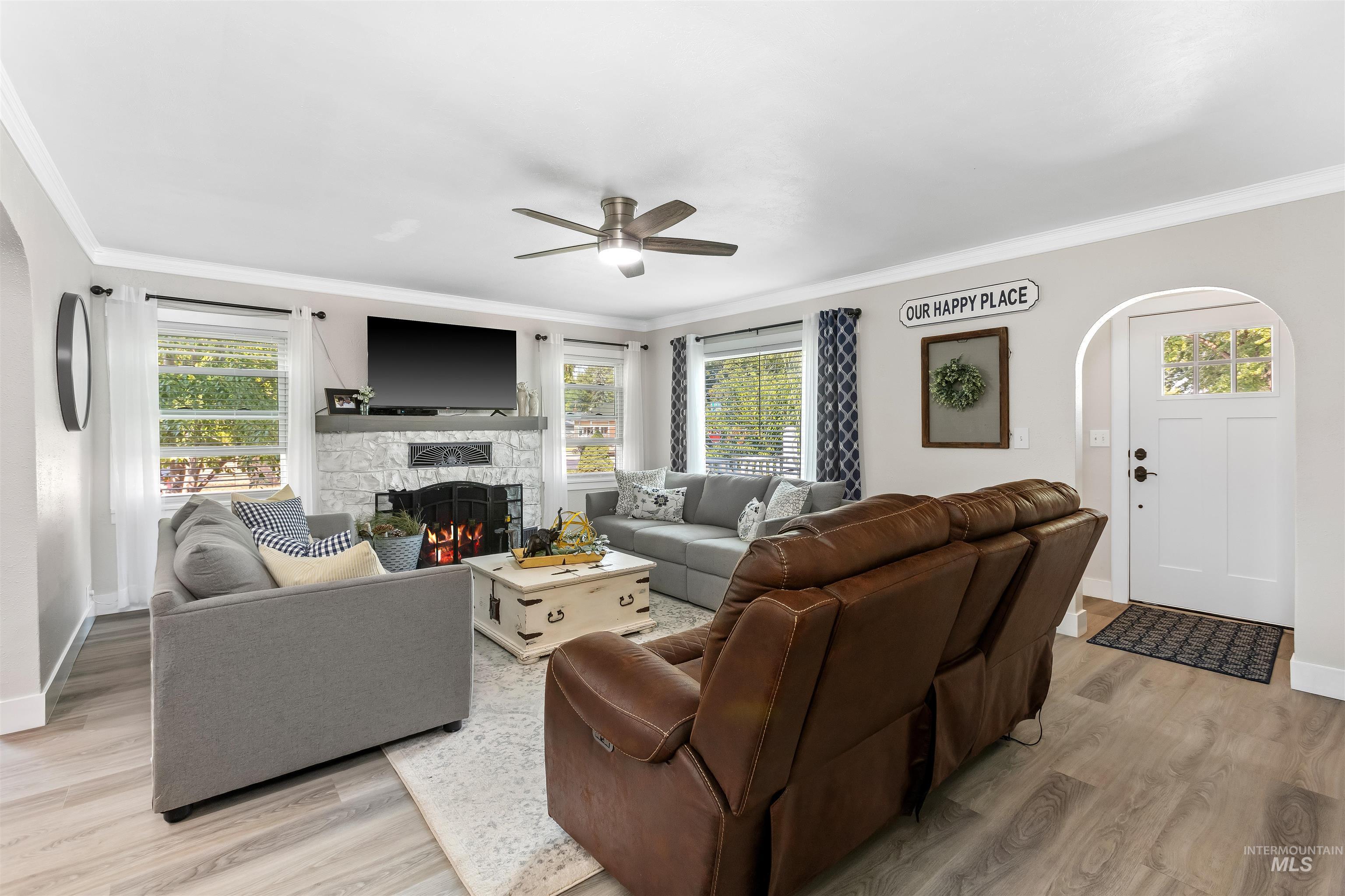 Living area featuring ornamental molding, a fireplace, light wood-type flooring, a ceiling fan, and arched walkways
