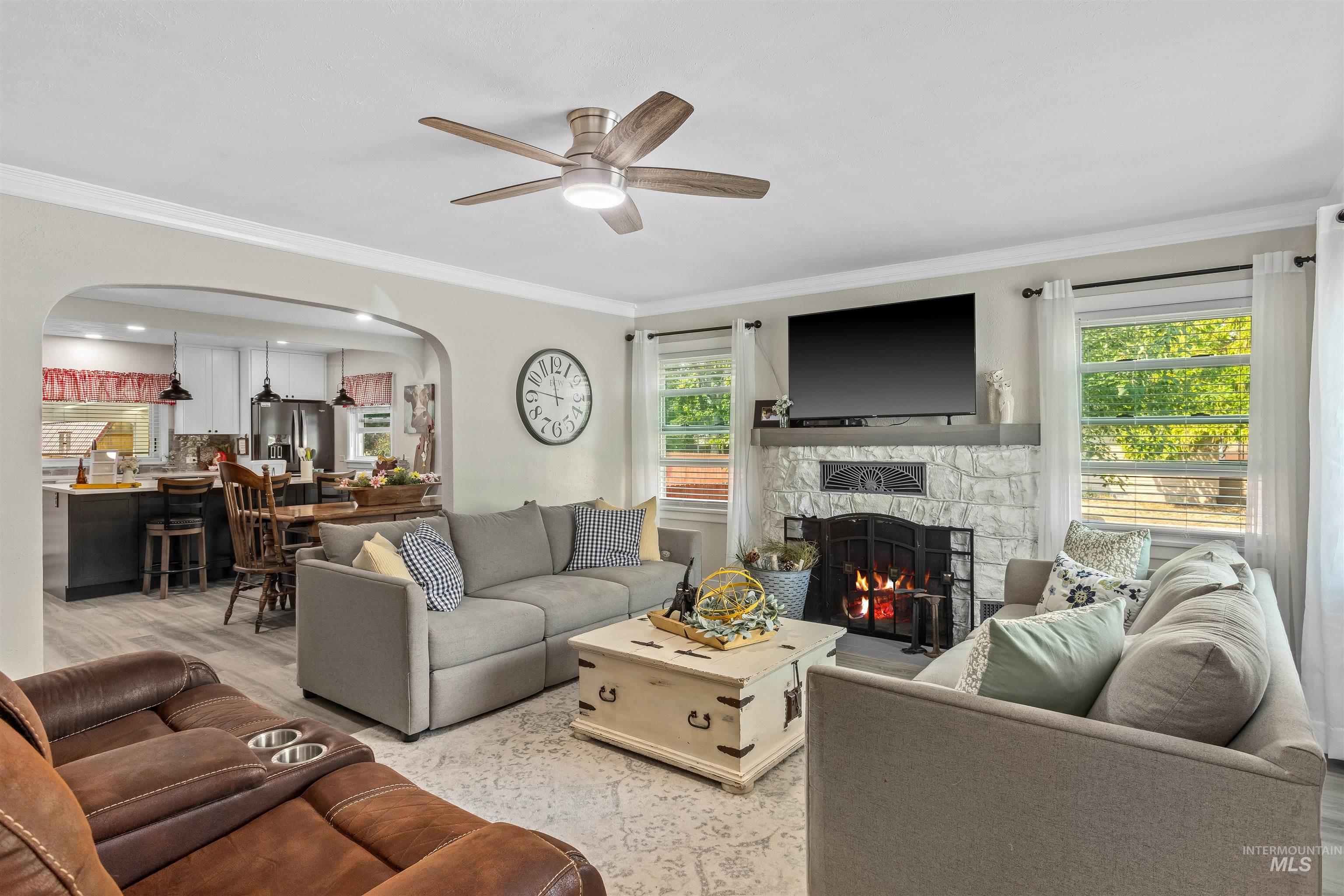 Living area featuring light wood-style floors, crown molding, arched walkways, a fireplace, and ceiling fan