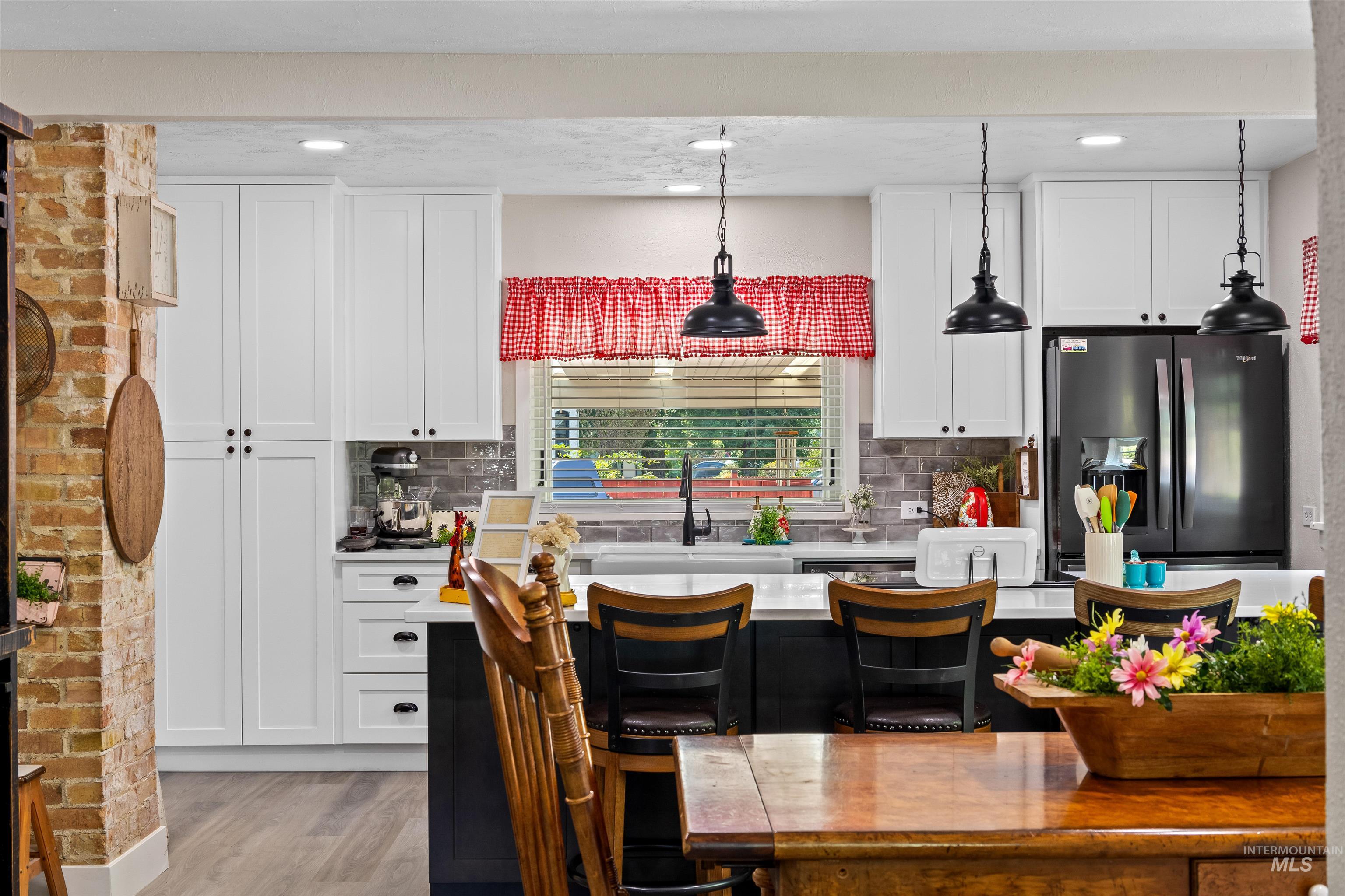 Kitchen featuring hanging light fixtures, white cabinetry, a breakfast bar, stainless steel refrigerator with ice dispenser, and tasteful backsplash
