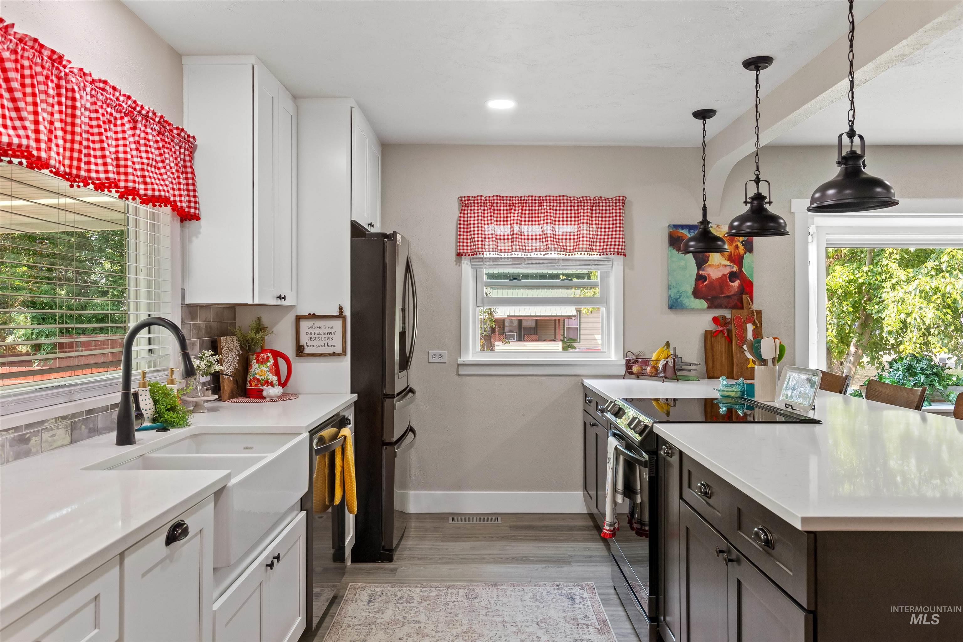 Kitchen featuring stainless steel appliances, light wood-type flooring, tasteful backsplash, white cabinetry, and hanging light fixtures