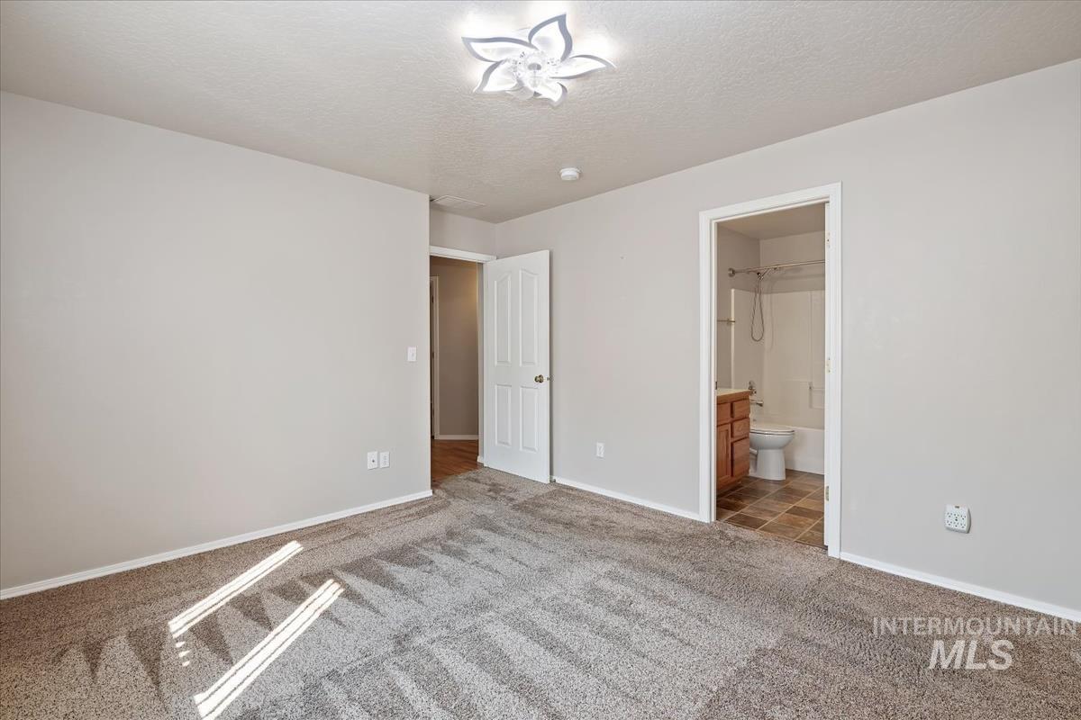 Unfurnished bedroom with a textured ceiling, light colored carpet, and ensuite bathroom