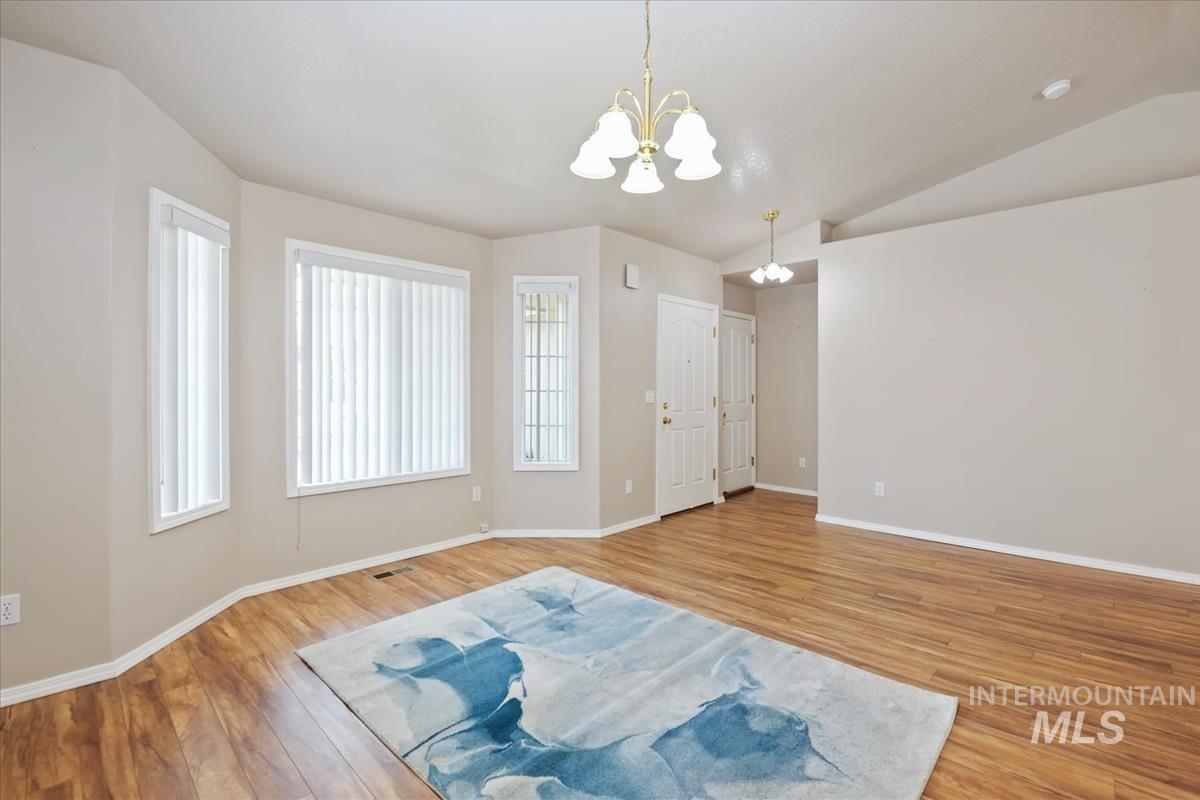 Empty room featuring a chandelier, light wood-style floors, and lofted ceiling
