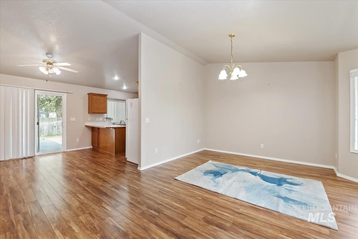 Unfurnished dining area featuring light wood-style floors, a chandelier, ceiling fan, and lofted ceiling