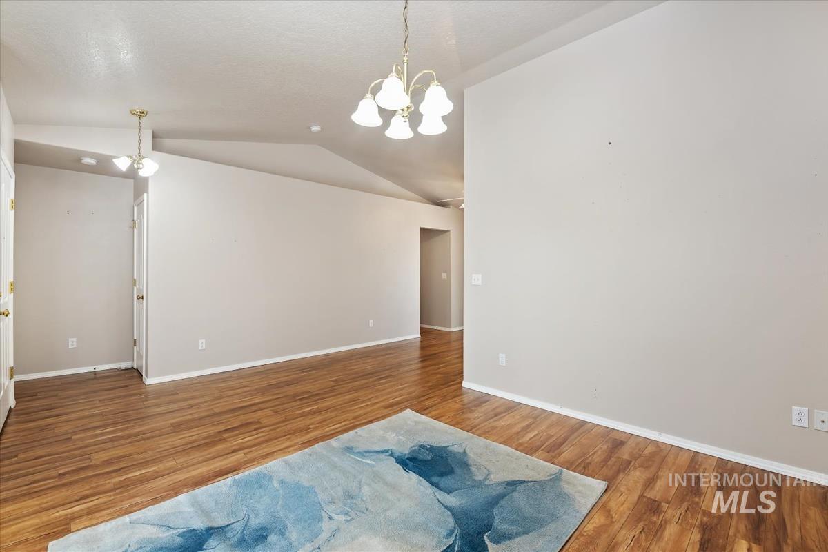 Empty room with a chandelier, vaulted ceiling, and wood finished floors