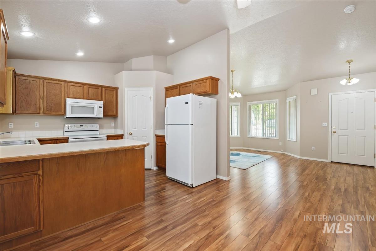 Kitchen with white appliances, brown cabinetry, a peninsula, light countertops, and vaulted ceiling