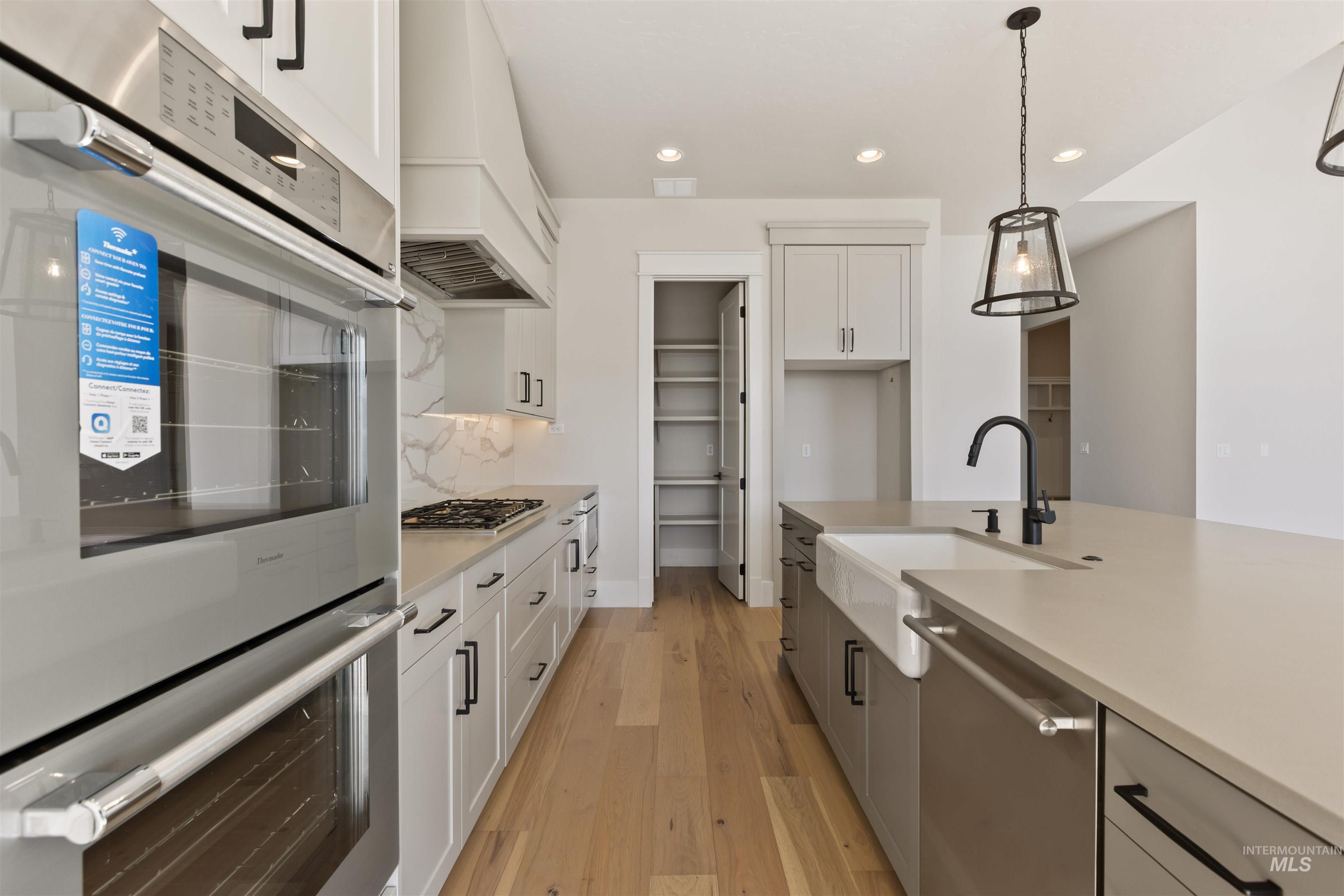 Kitchen with appliances with stainless steel finishes, pendant lighting, light countertops, light wood finished floors, and recessed lighting