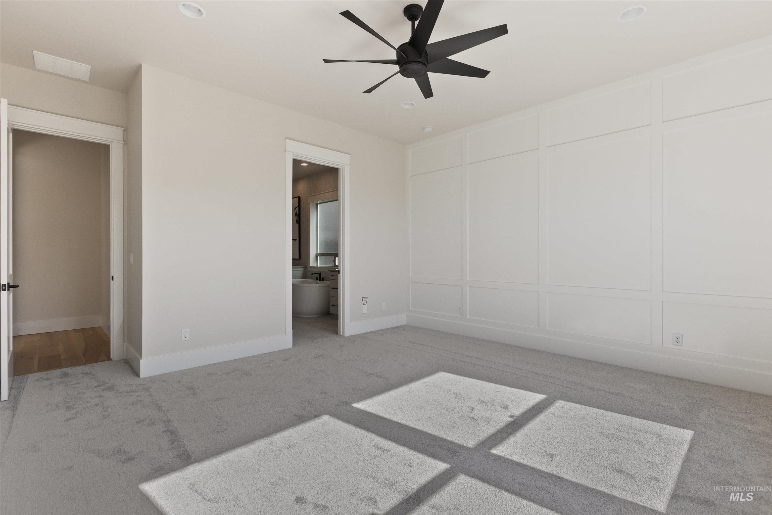 Unfurnished bedroom with light carpet, ensuite bathroom, and a ceiling fan