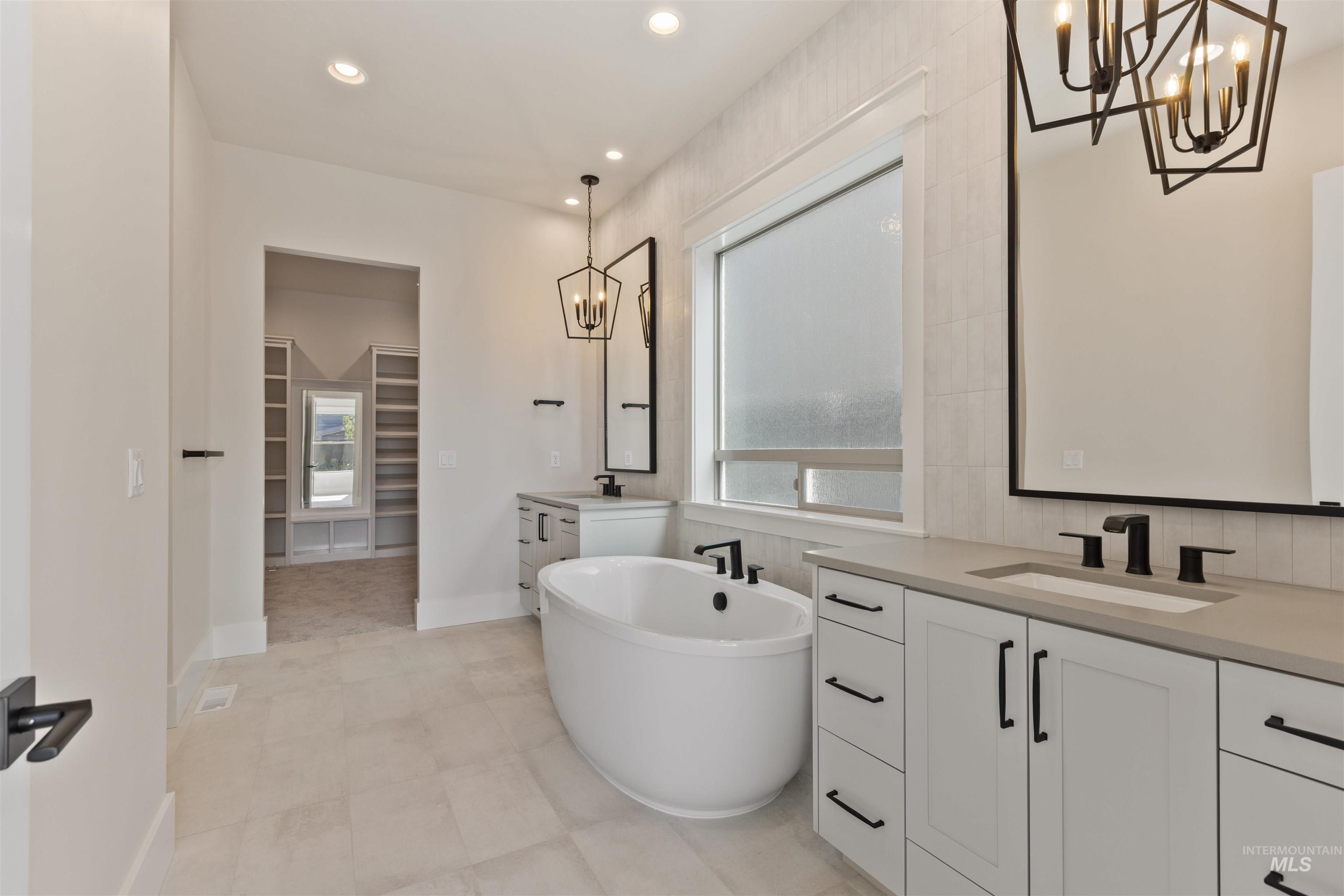 Full bath with a chandelier, two vanities, a spacious closet, a soaking tub, and recessed lighting