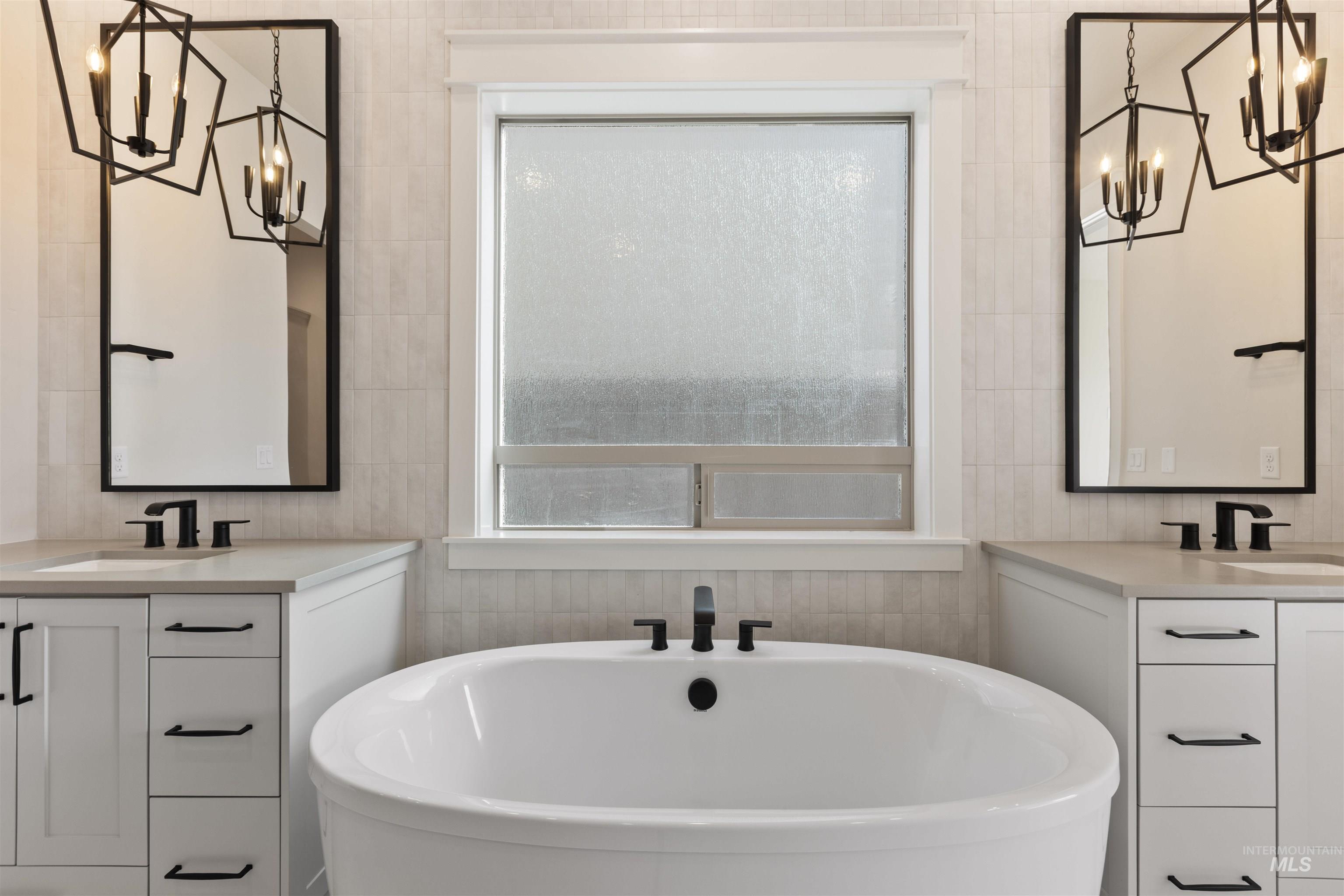 Full bath featuring a chandelier, a freestanding bath, and two vanities