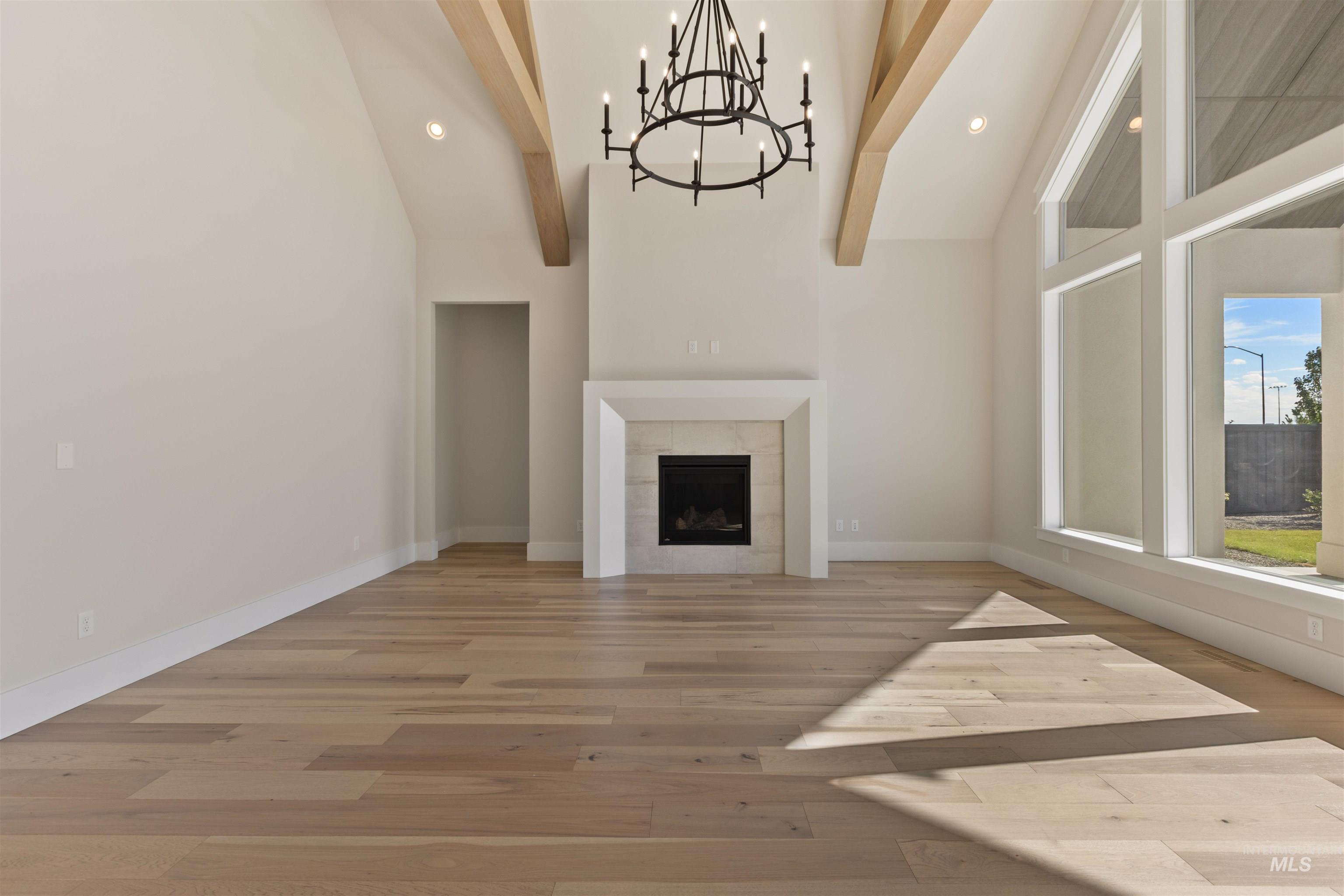Unfurnished living room featuring light wood finished floors, a chandelier, beam ceiling, high vaulted ceiling, and recessed lighting