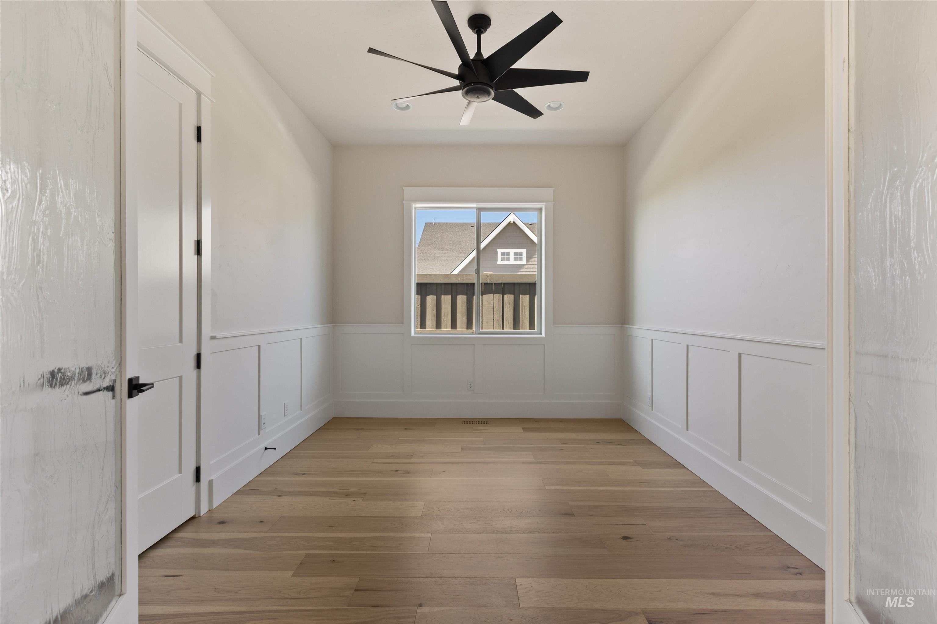 Unfurnished room with a wainscoted wall, light wood-style flooring, and ceiling fan