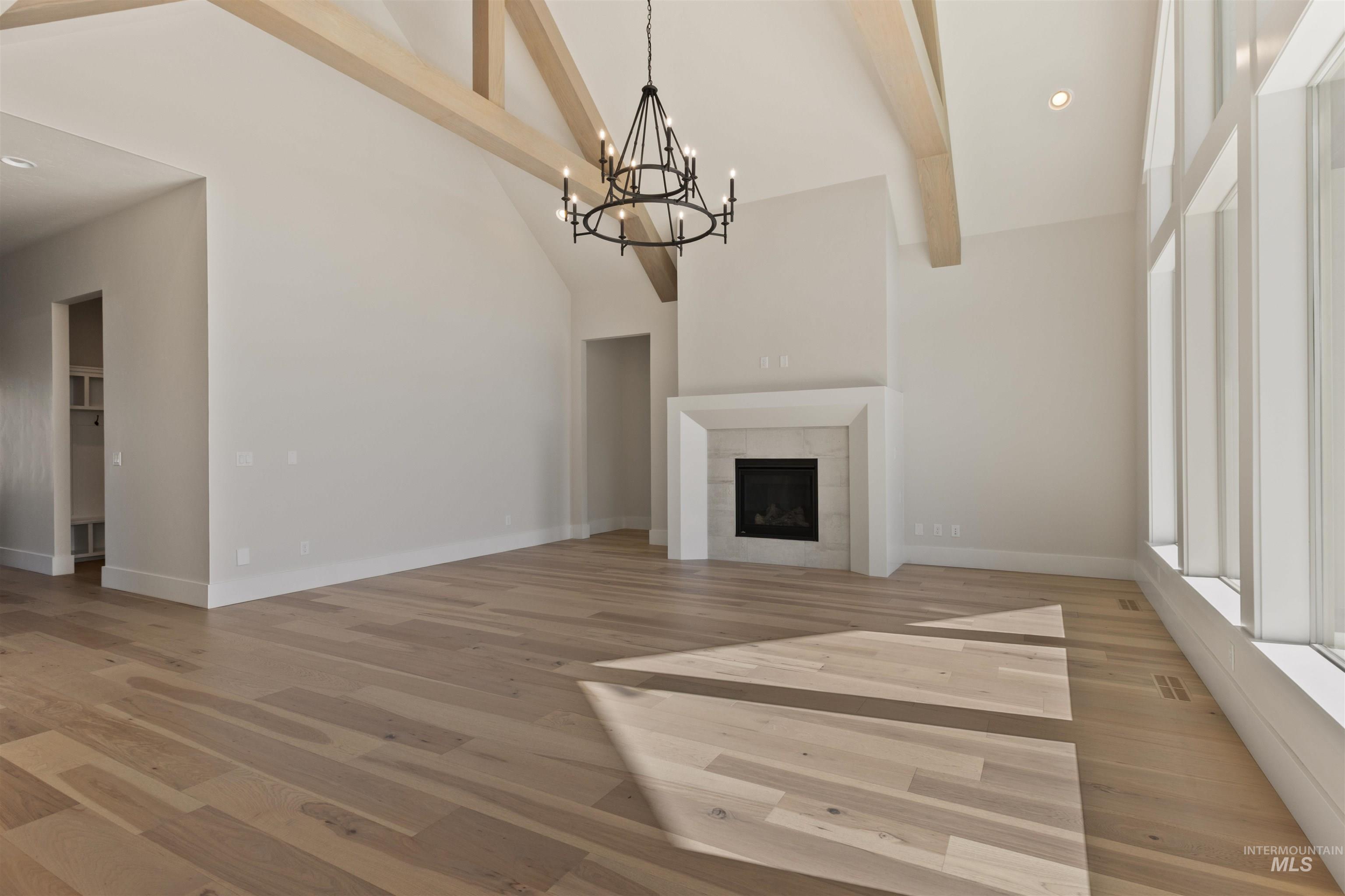 Unfurnished living room featuring high vaulted ceiling, beamed ceiling, light wood finished floors, a chandelier, and a fireplace