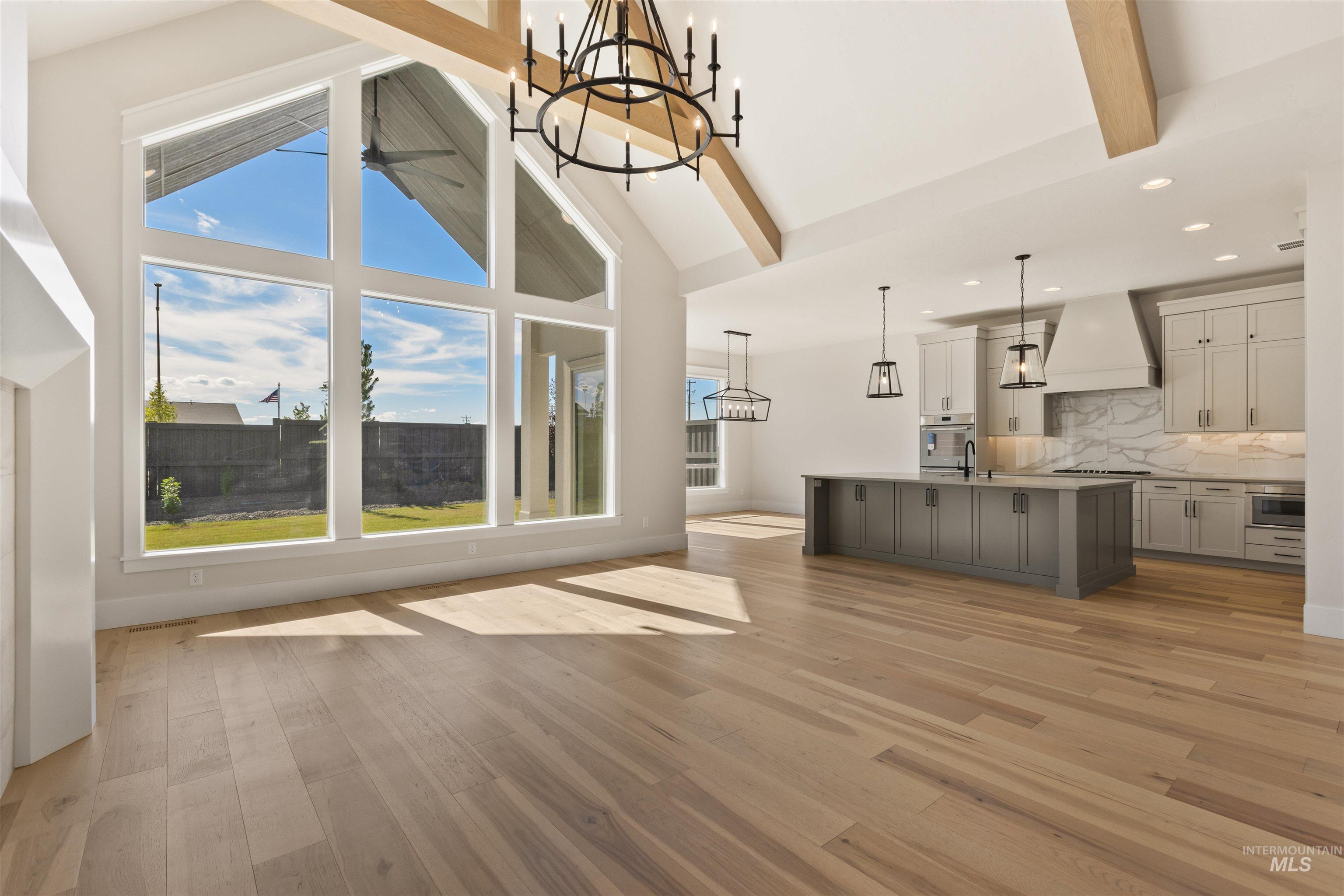 Unfurnished living room featuring a chandelier, recessed lighting, beam ceiling, light wood-style floors, and high vaulted ceiling