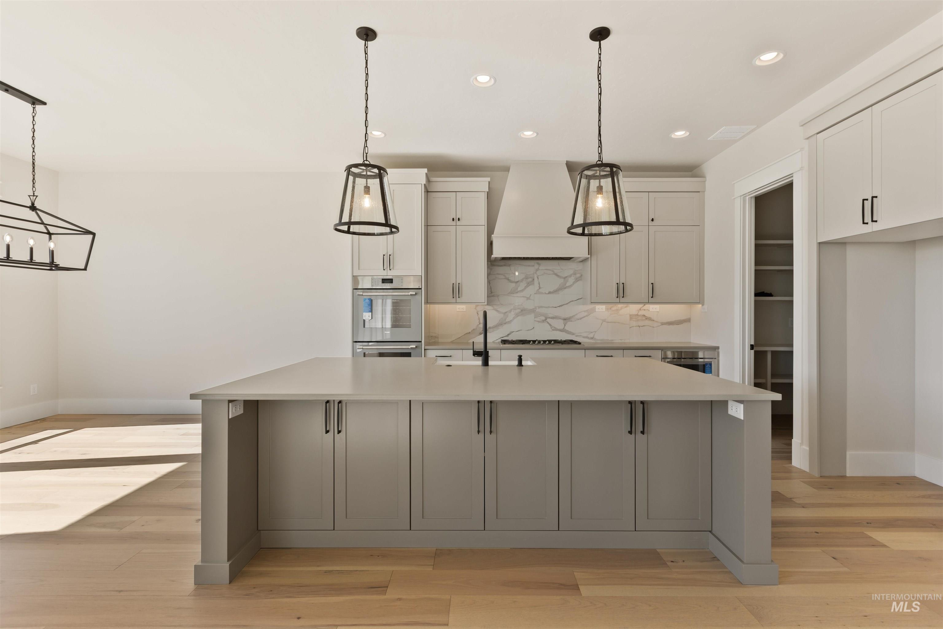 Kitchen with decorative backsplash, white cabinetry, an island with sink, light countertops, and custom exhaust hood