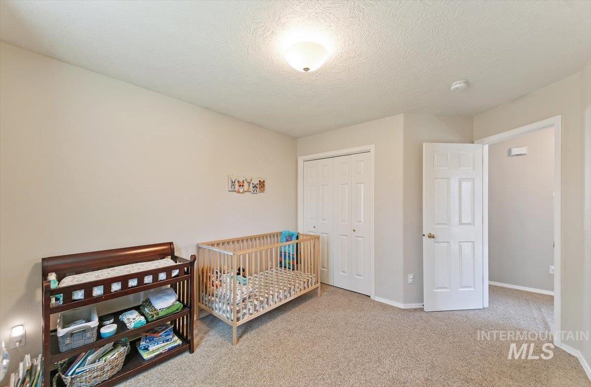 Bedroom with a textured ceiling, light colored carpet, a closet, and a nursery area