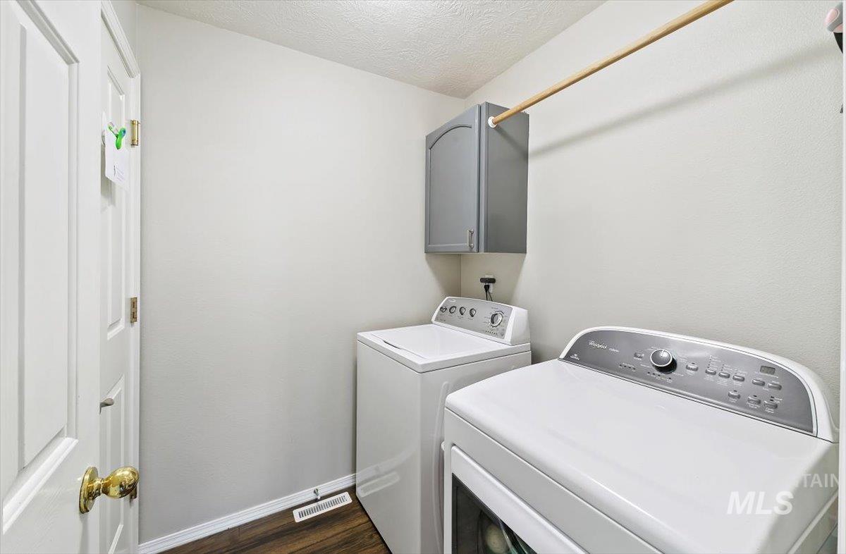 Laundry area with dark wood-type flooring, washer and clothes dryer, a textured ceiling, and cabinet space