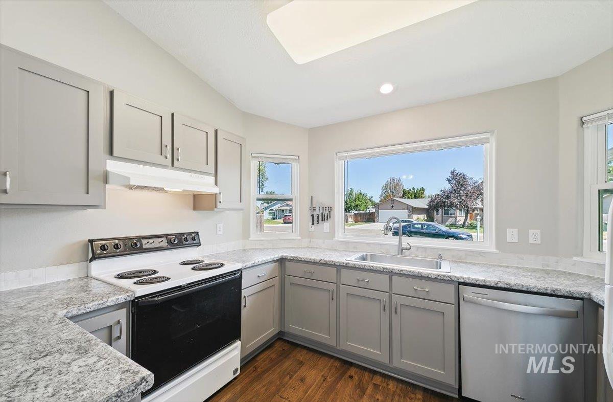 Kitchen featuring gray cabinetry, white range with electric stovetop, stainless steel dishwasher, dark wood finished floors, and under cabinet range hood