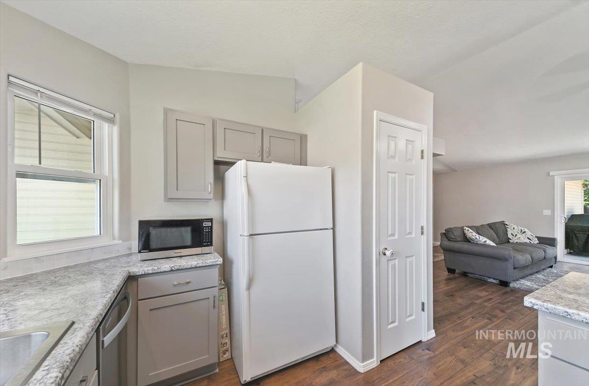 Kitchen featuring appliances with stainless steel finishes, gray cabinets, dark wood-style flooring, open floor plan, and light stone countertops