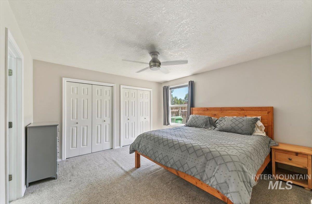 Carpeted bedroom featuring multiple closets, a textured ceiling, and ceiling fan