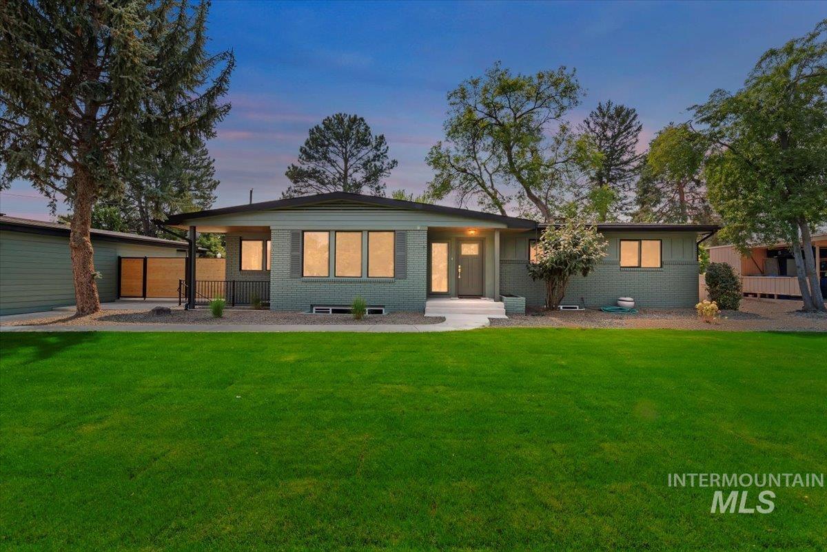 Back of house at dusk with brick siding, a lawn, and a patio