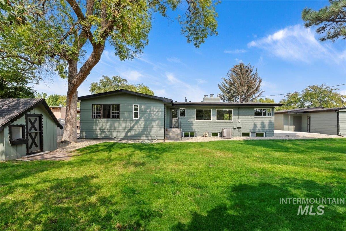 Back of property with a storage unit, a patio, a yard, and brick siding