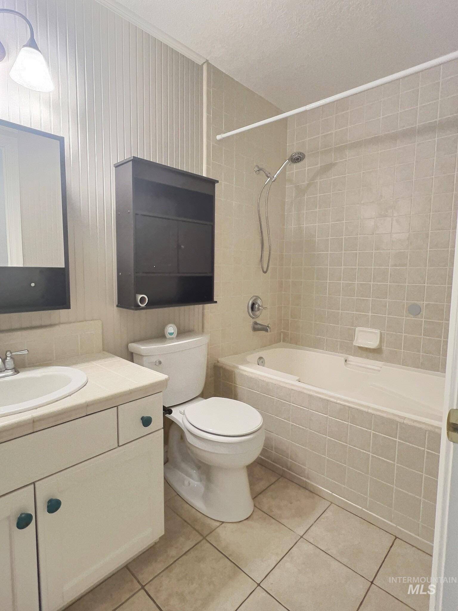 Bathroom featuring tiled shower / bath, vanity, light tile patterned floors, and a textured ceiling