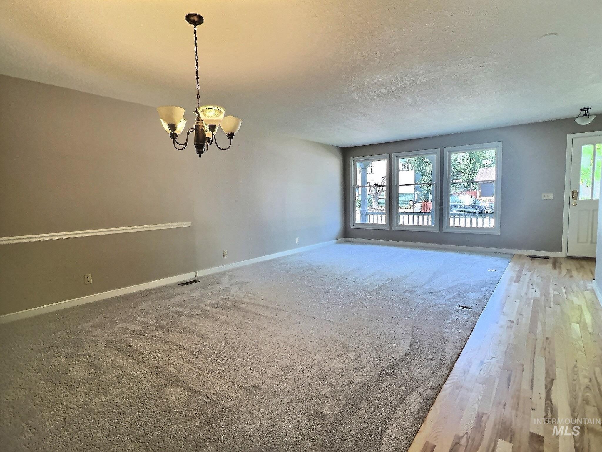 Spare room featuring a textured ceiling, a chandelier, and wood finished floors
