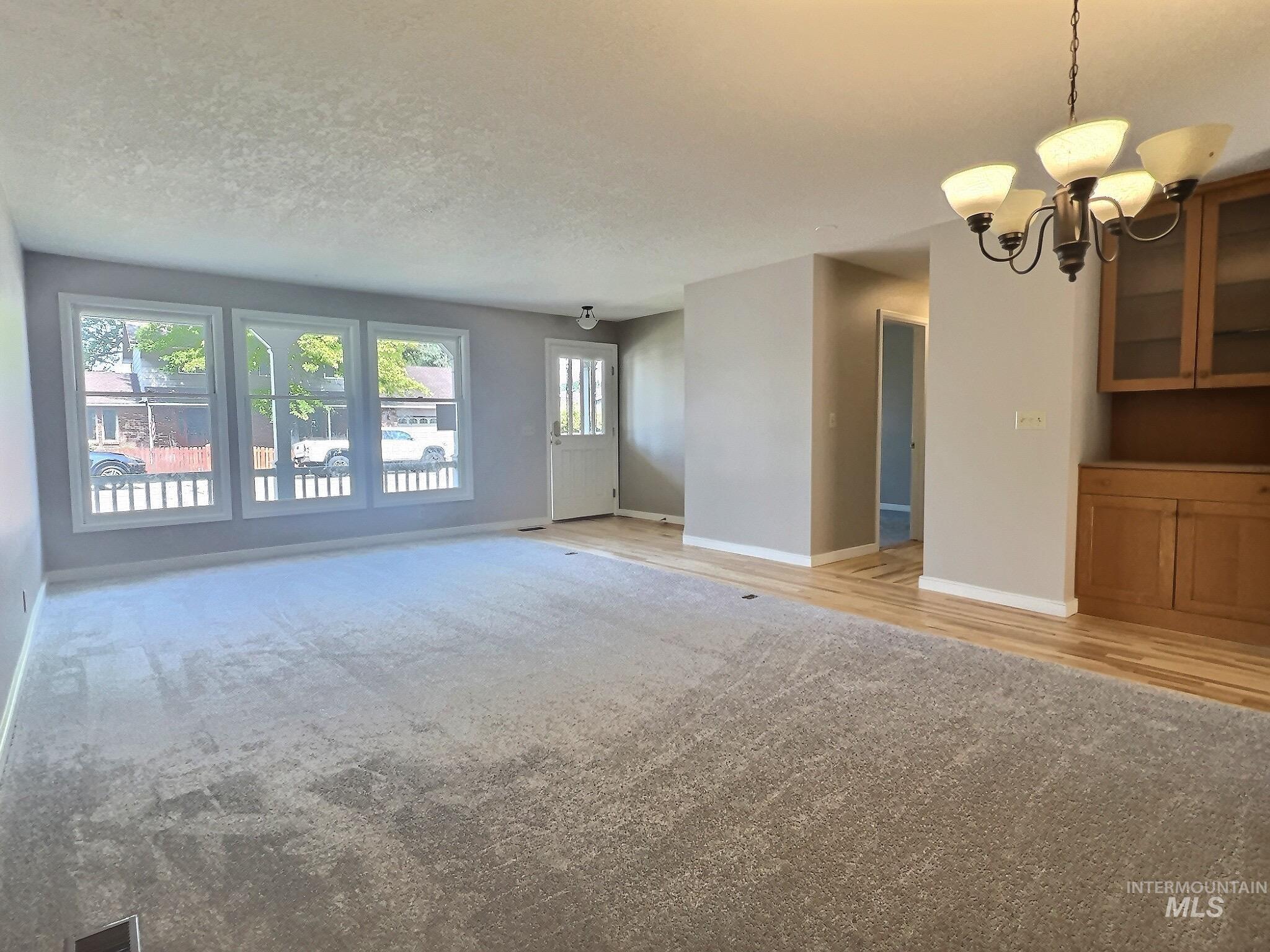 Unfurnished living room featuring a chandelier, a textured ceiling, light carpet, and light wood-type flooring