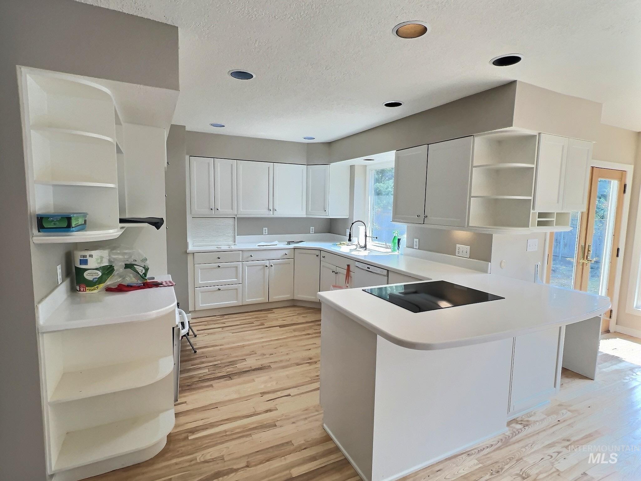Kitchen featuring open shelves, white cabinets, a peninsula, light wood-type flooring, and a textured ceiling