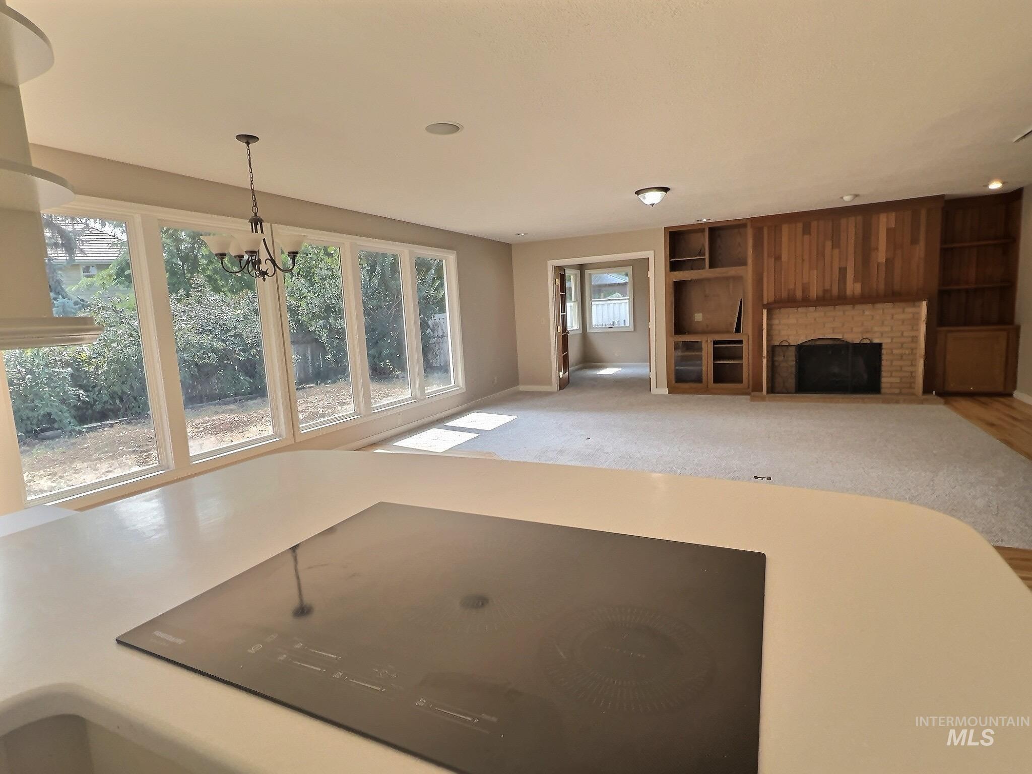 Unfurnished living room with a brick fireplace, a chandelier, and carpet floors