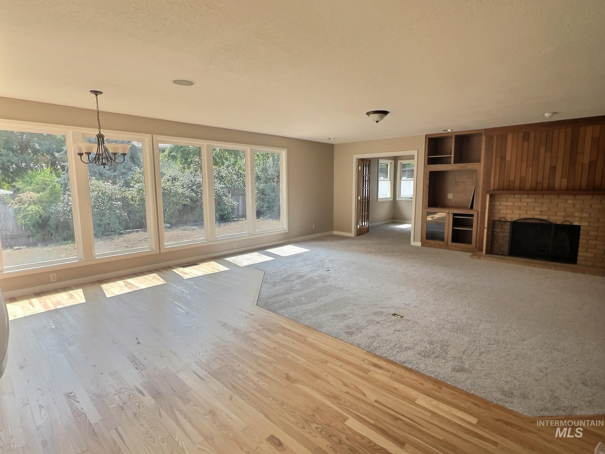 Unfurnished living room featuring a brick fireplace, a chandelier, light wood-style flooring, and light colored carpet