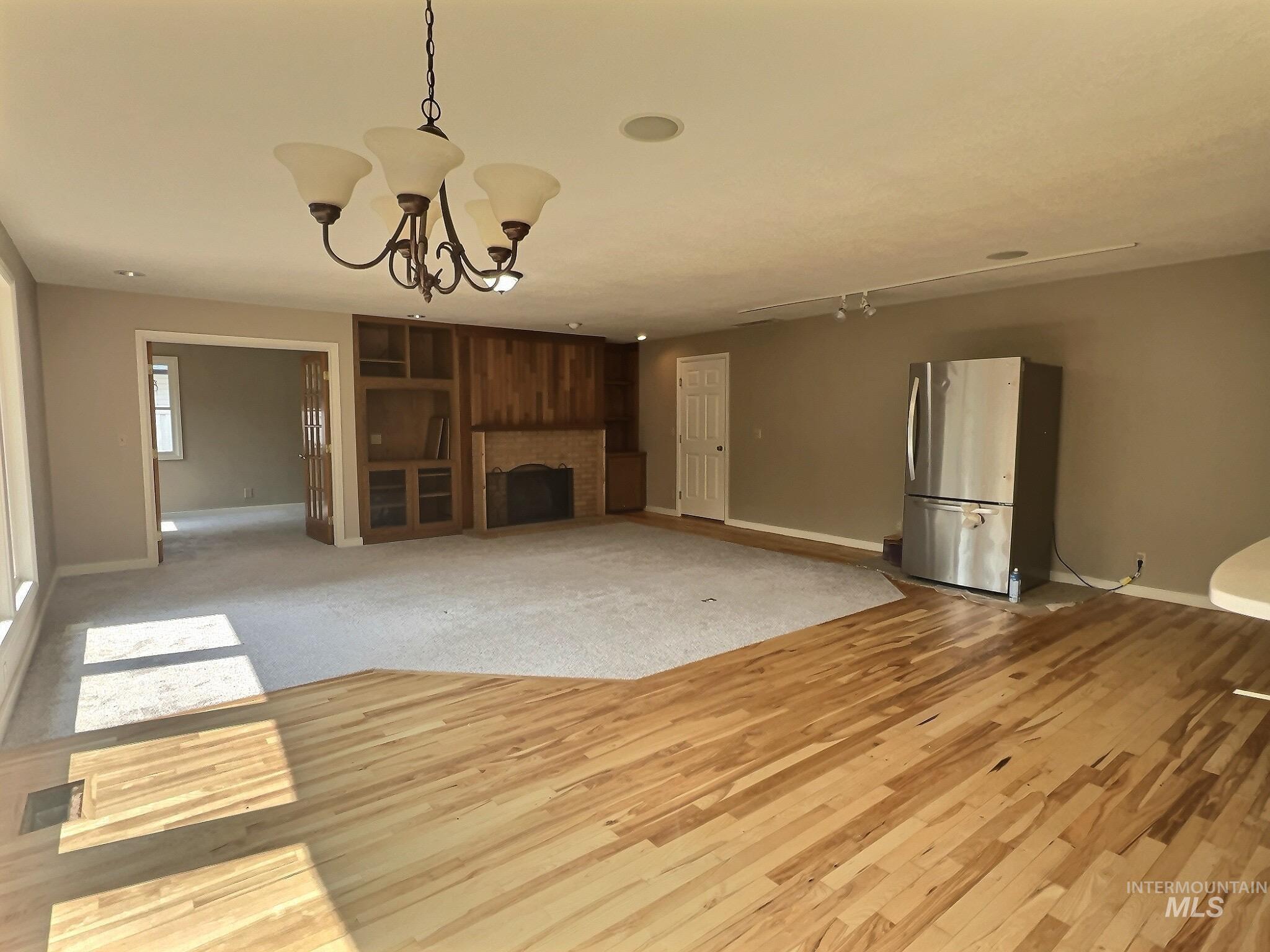 Unfurnished living room featuring a chandelier, a brick fireplace, and light wood-style flooring