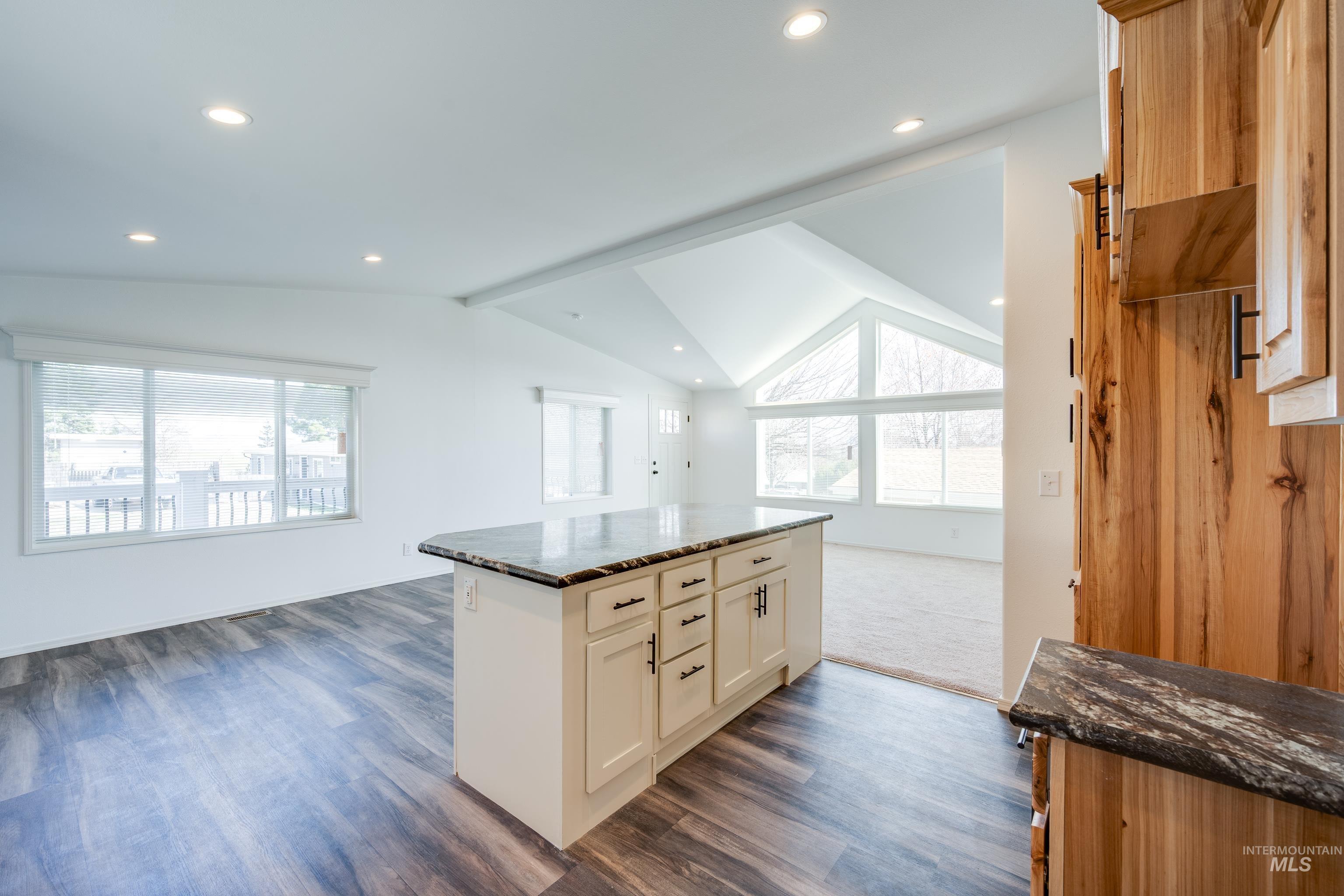Kitchen with dark stone counters, a kitchen island, open floor plan, recessed lighting, and dark wood-style floors