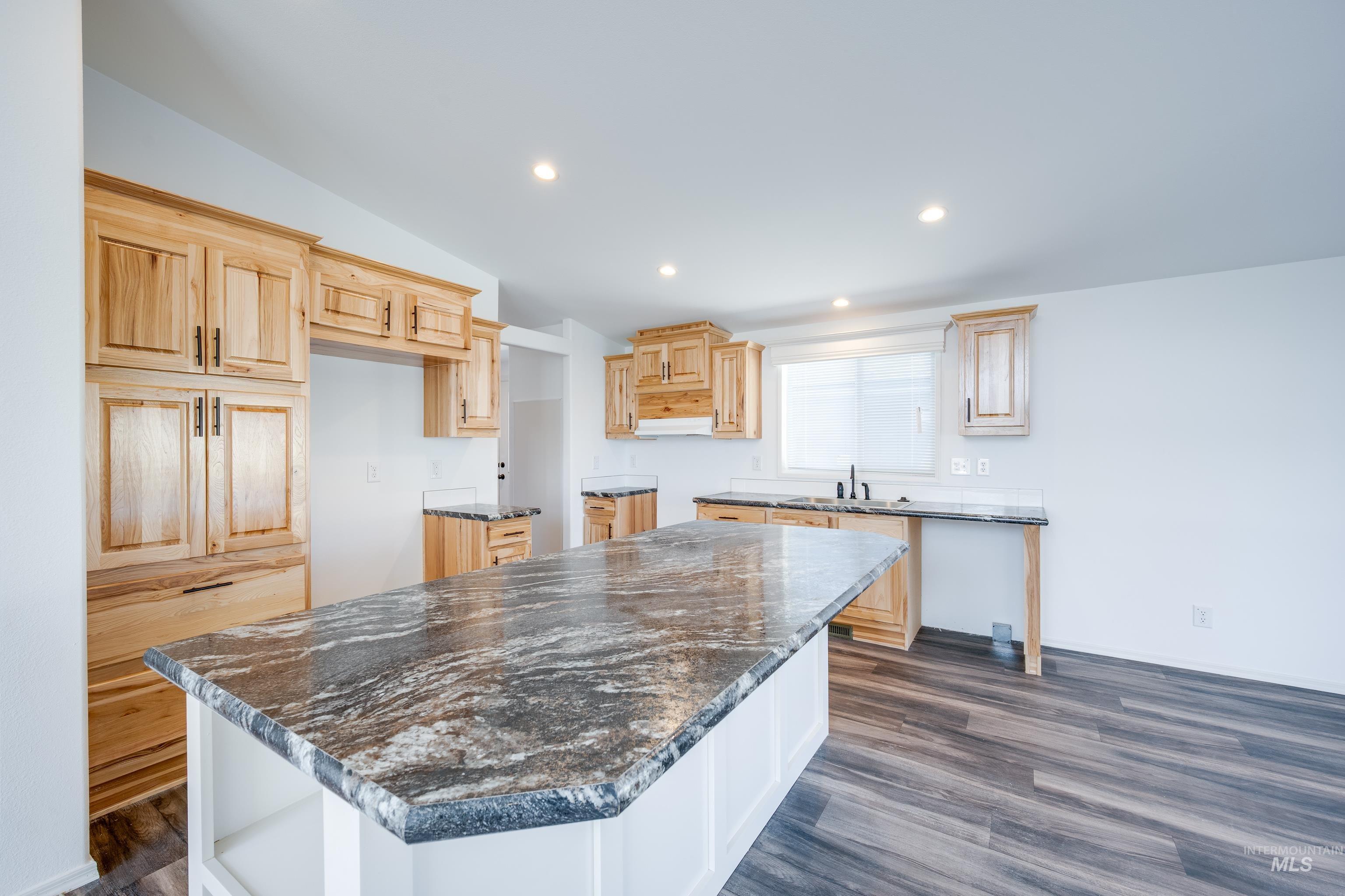 Kitchen featuring recessed lighting, dark wood-type flooring, light brown cabinetry, a center island, and lofted ceiling