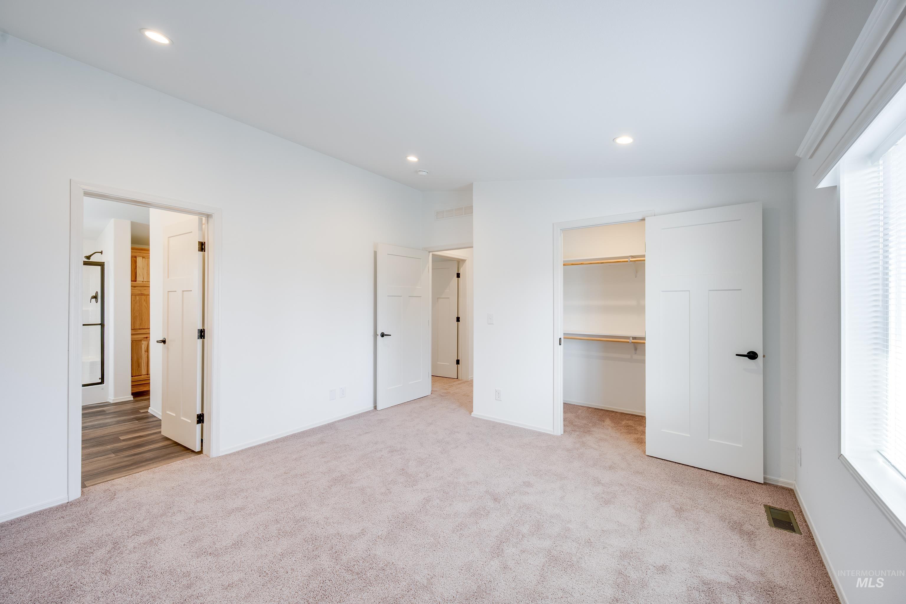Unfurnished bedroom with light colored carpet, multiple windows, recessed lighting, and a walk in closet