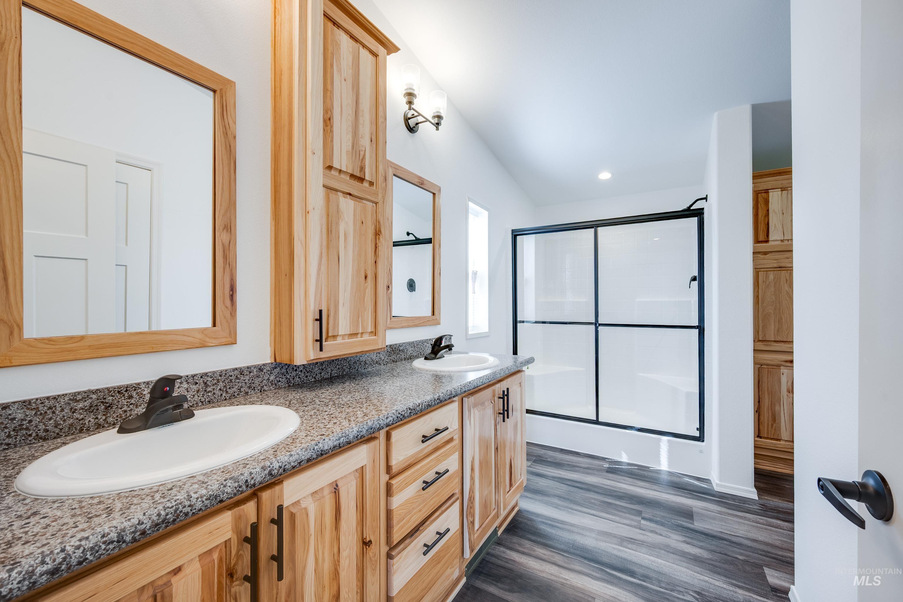 Full bath with a shower stall, double vanity, dark wood-style flooring, and recessed lighting
