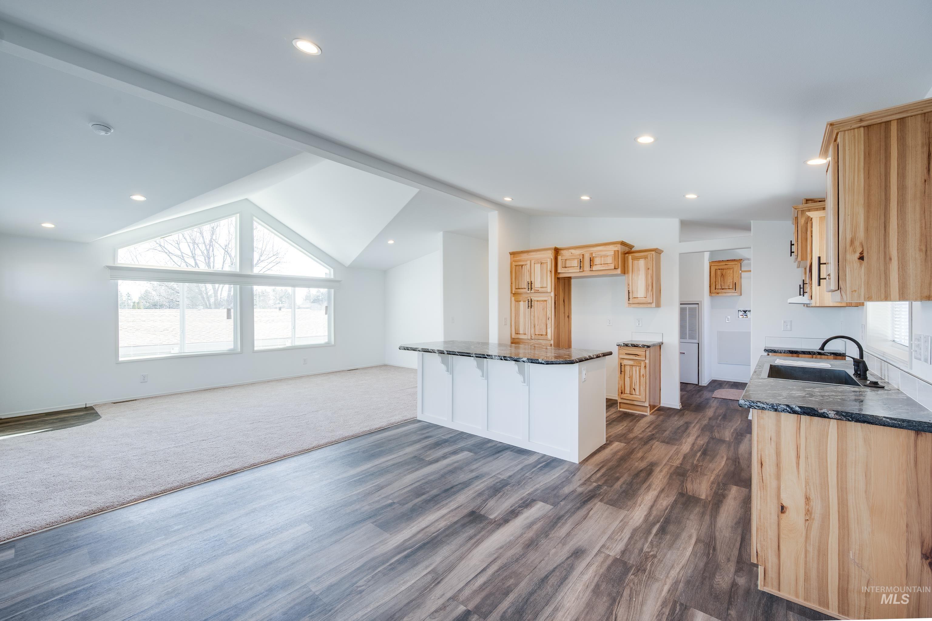 Kitchen featuring vaulted ceiling, open floor plan, dark stone counters, a kitchen bar, and light brown cabinetry