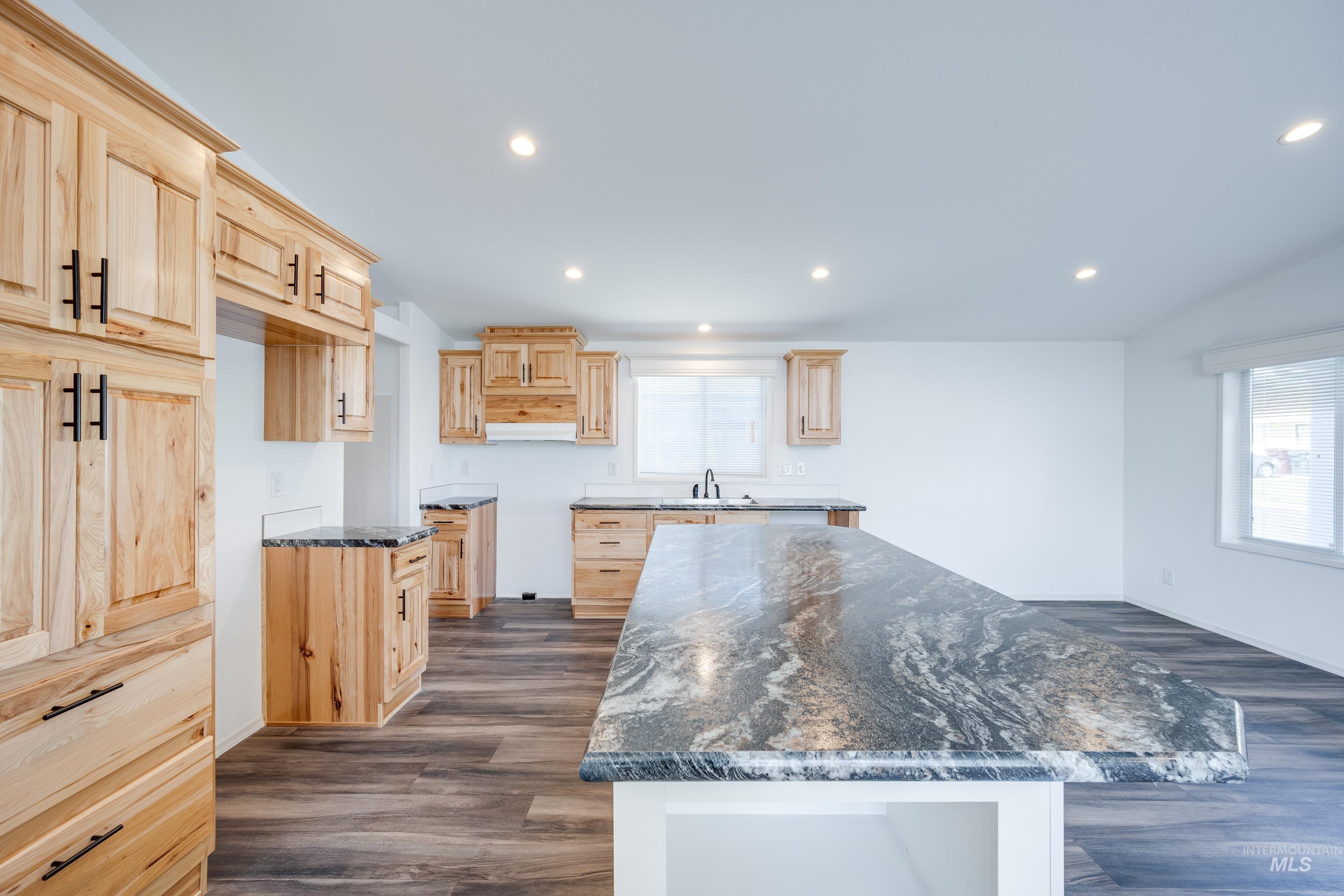 Kitchen featuring light brown cabinetry, dark stone counters, dark wood-style flooring, recessed lighting, and a center island